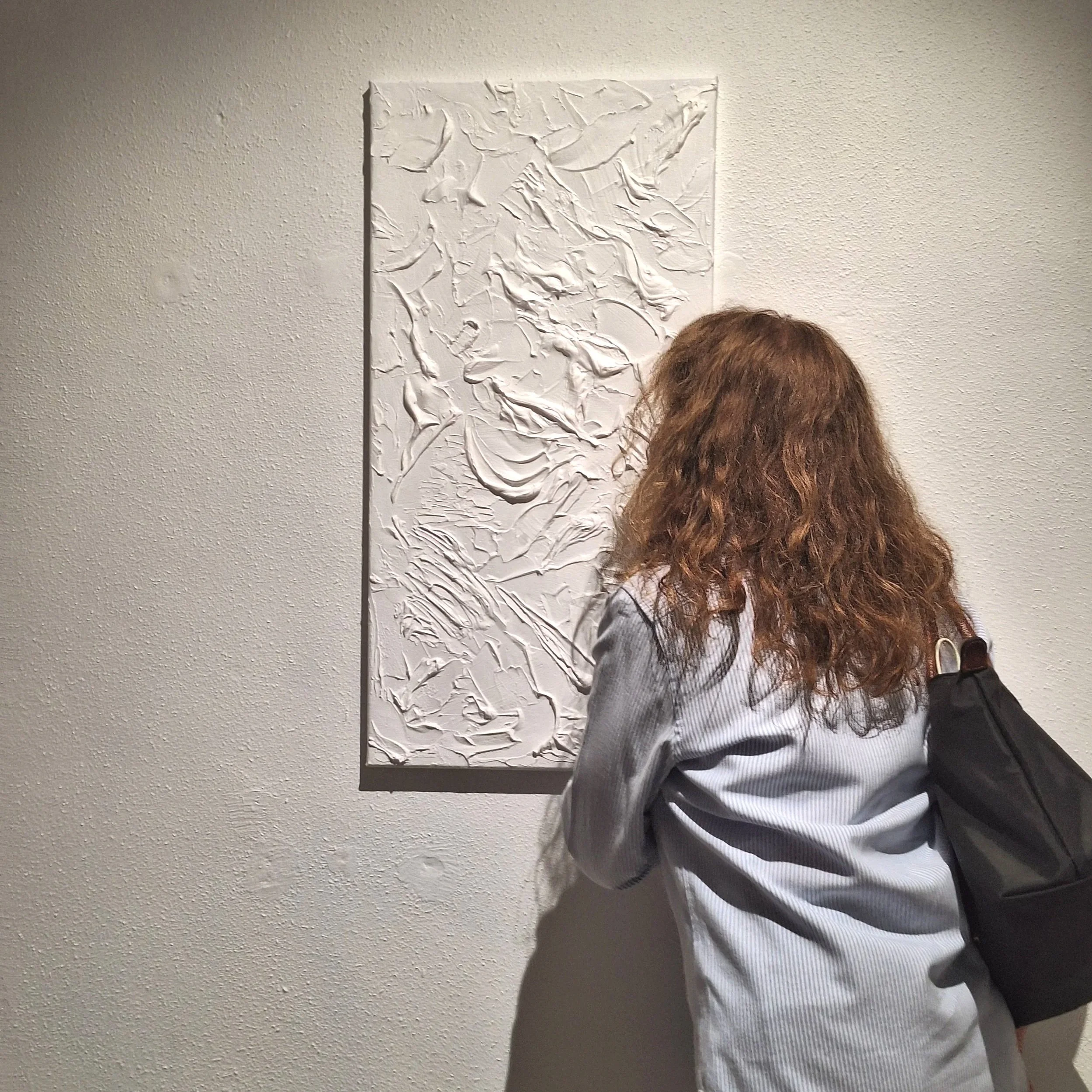 A woman leans into smell a scented paintings, which is entirely white but highly textured.
