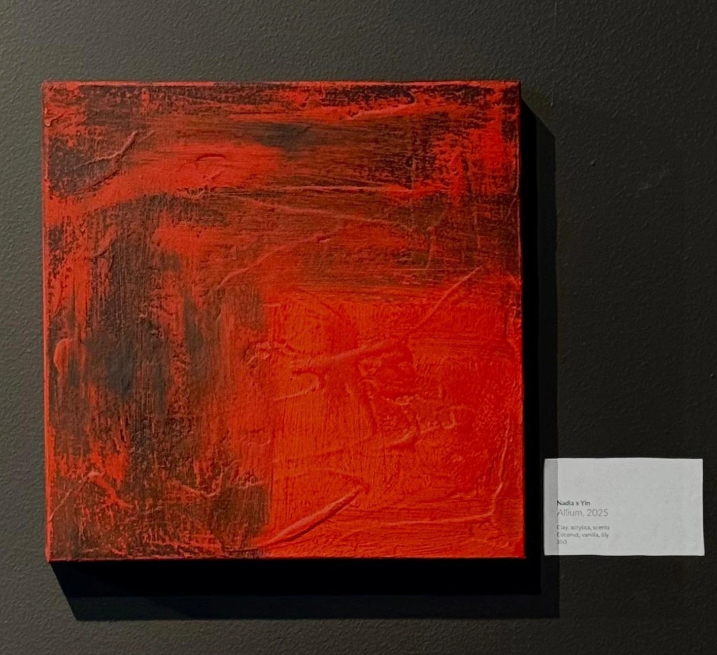 A heavily-scented red and black abstract painting displayed on a wall, with a label beside it.
