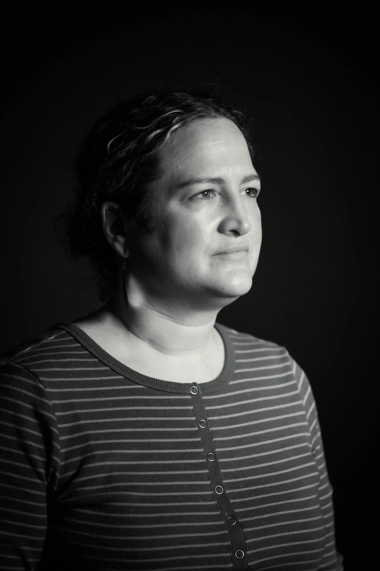 Person leaning against a wall with a red sweater and yellow earrings