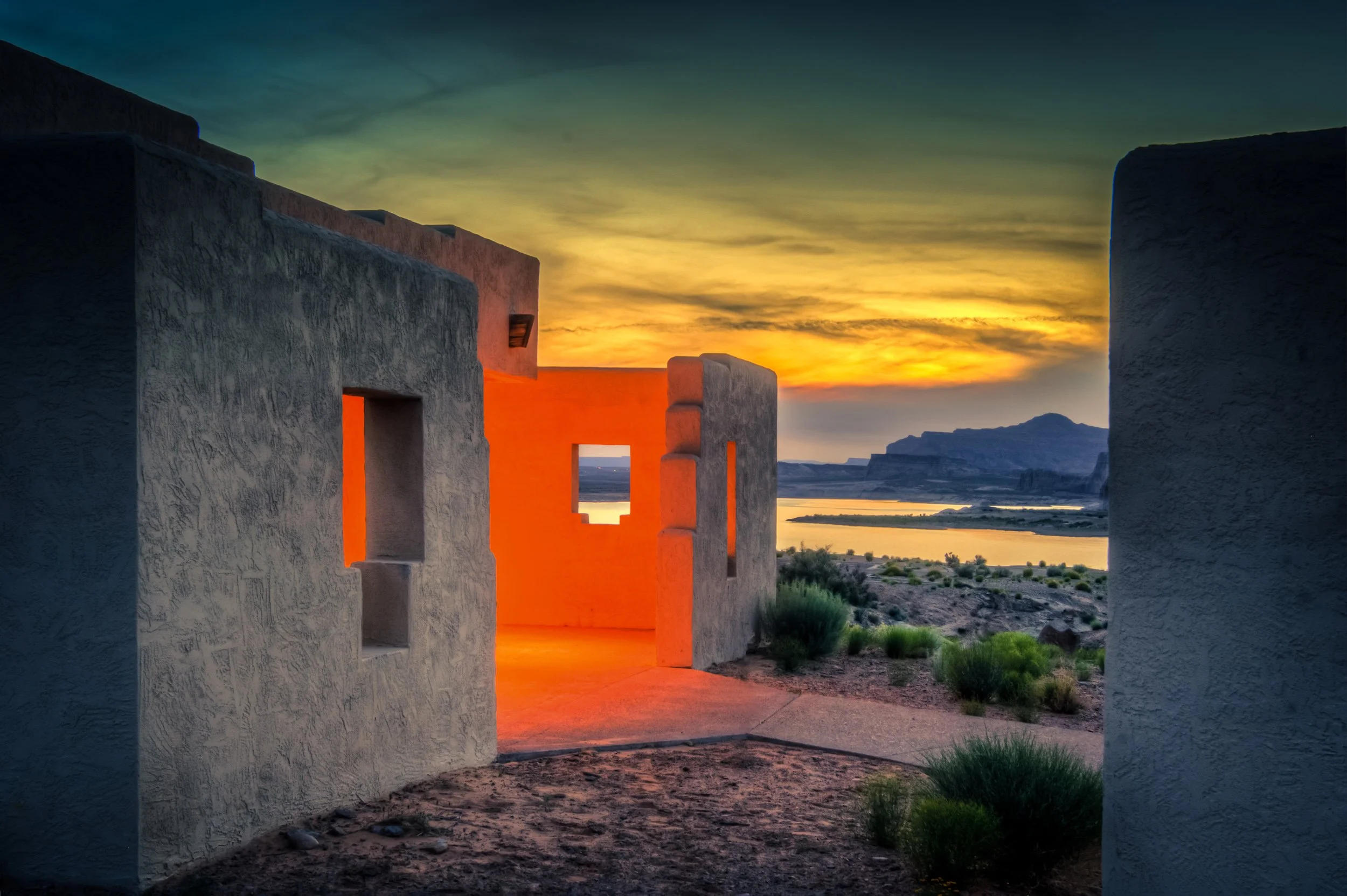 Scenic view of a sunset over a desert landscape framed by adobe-style structures with rectangular doorways and openings.