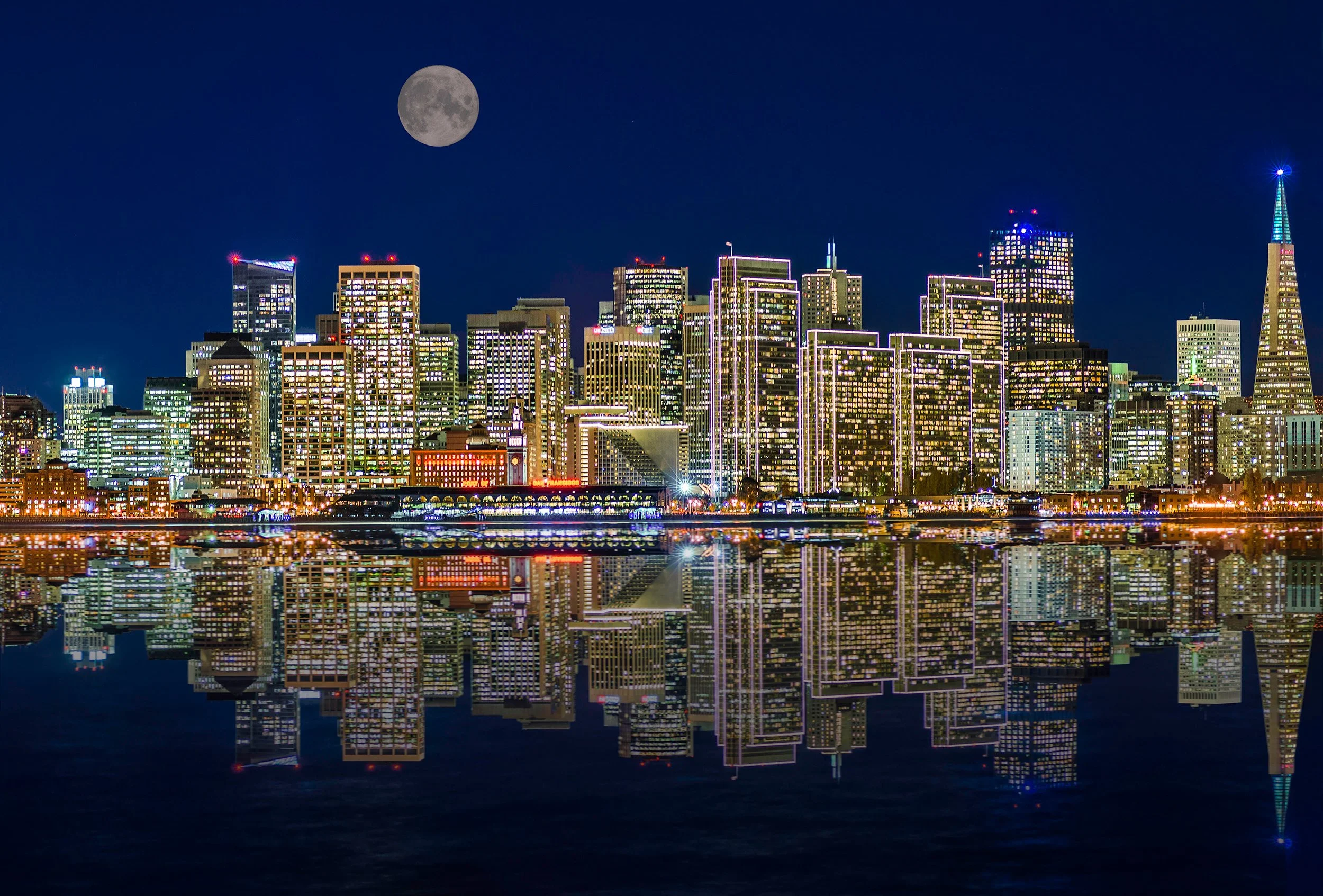 Nighttime city skyline with tall illuminated buildings reflecting on water, full moon in the clear dark sky.