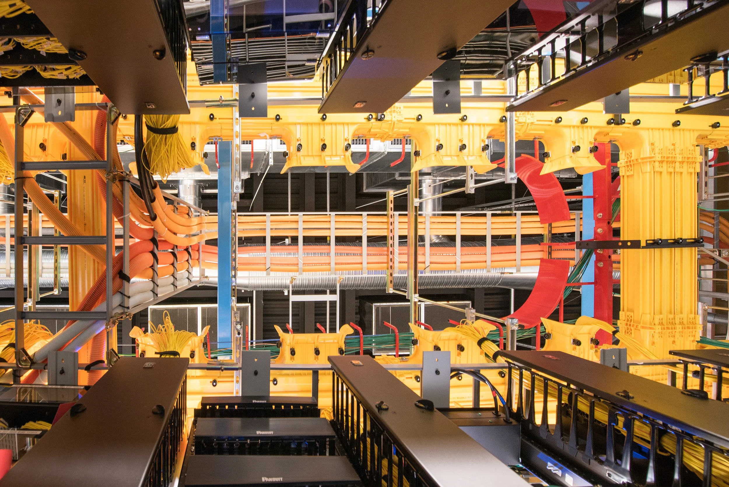 Interior view of a server or networking equipment room with various cables, servers, and hardware components, organized on racks with black metal frames.