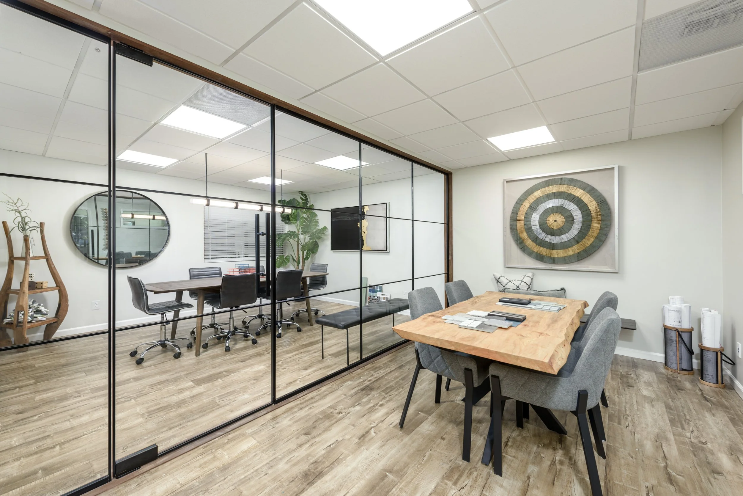 Office conference room with wooden table, gray chairs, wall art, and glass partition.