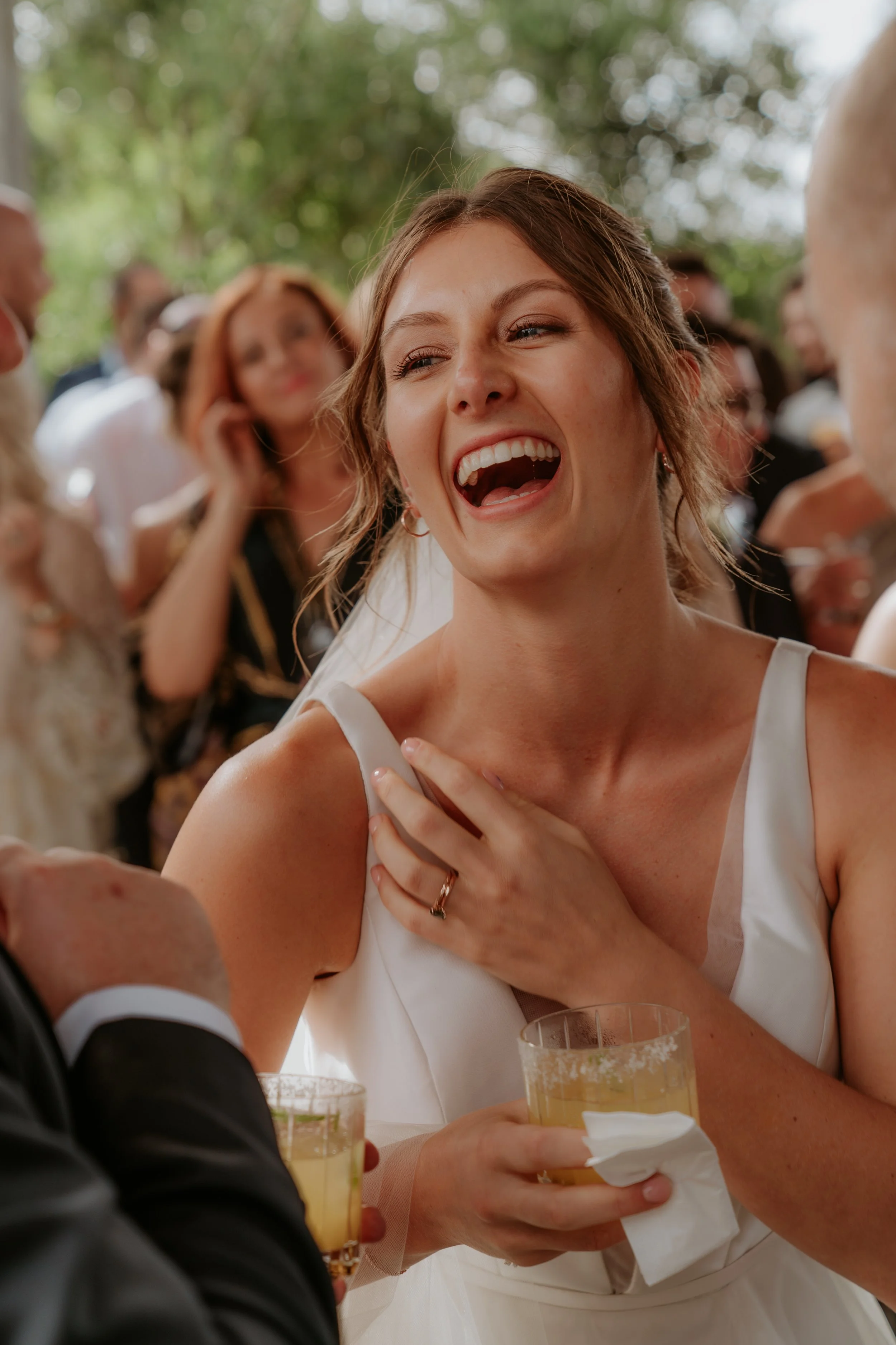 A bride during cocktail hour, holding a glass of champagne and laughing with guests.