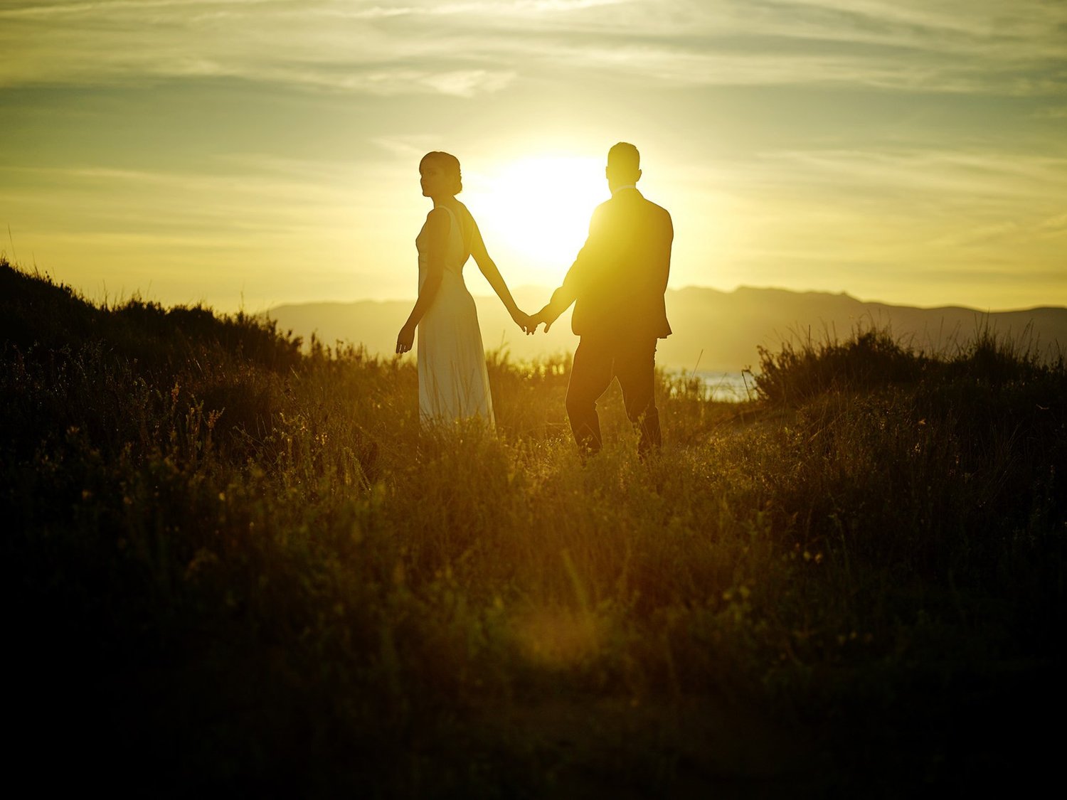 A couple walking through a field at sunset
