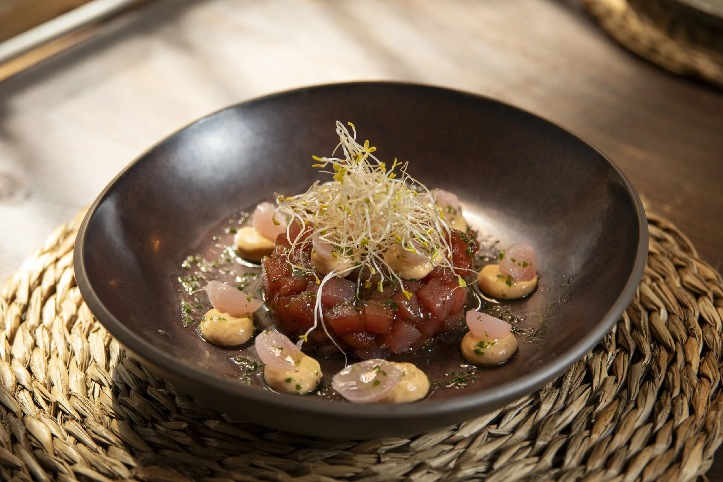 Plato de ceviche con pescado, cebolla y microverdes en un plato negro