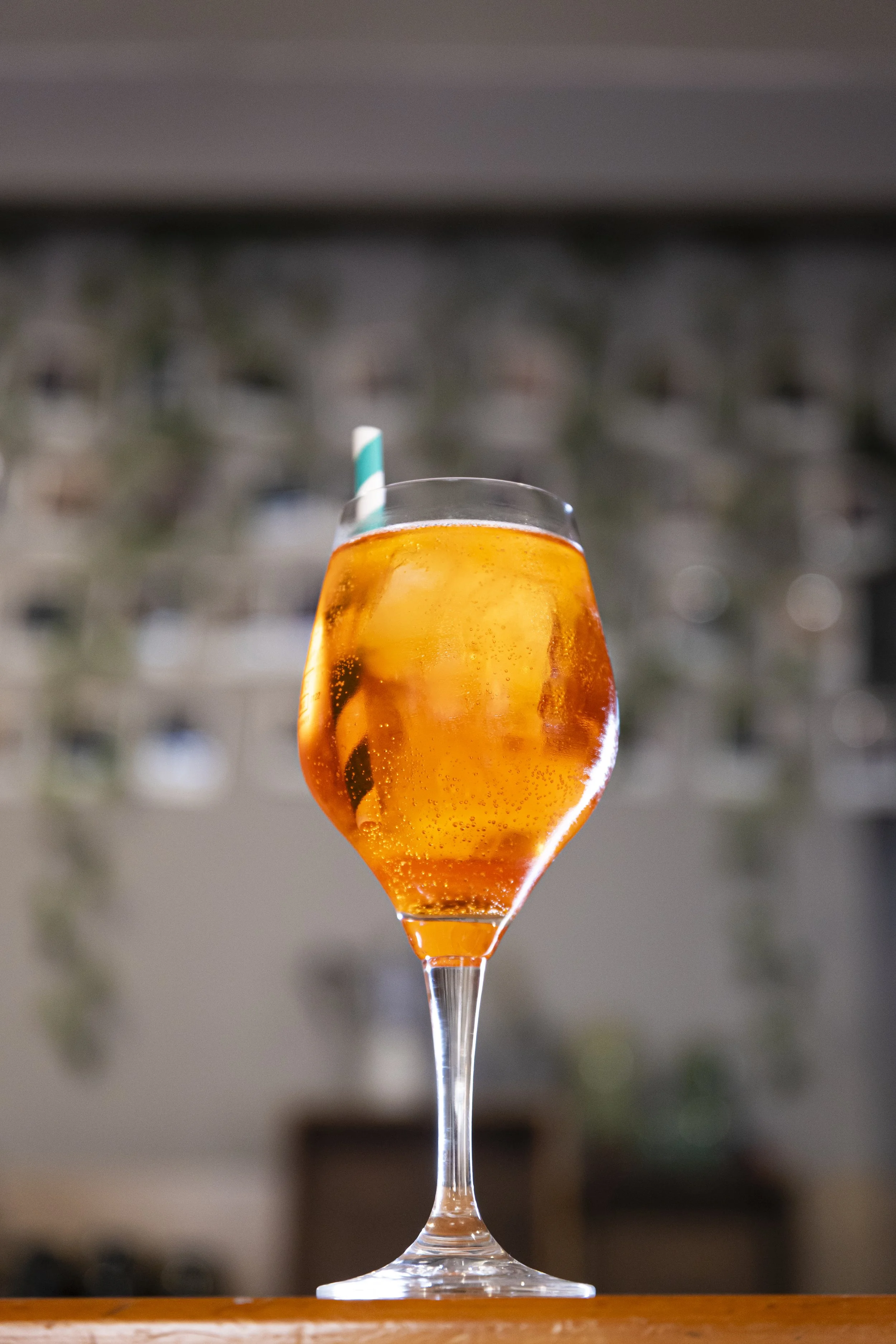 Vaso de cóctel con hielo y una pajilla de rayas azules y blancas, lleno de una bebida anaranjada con burbujas.