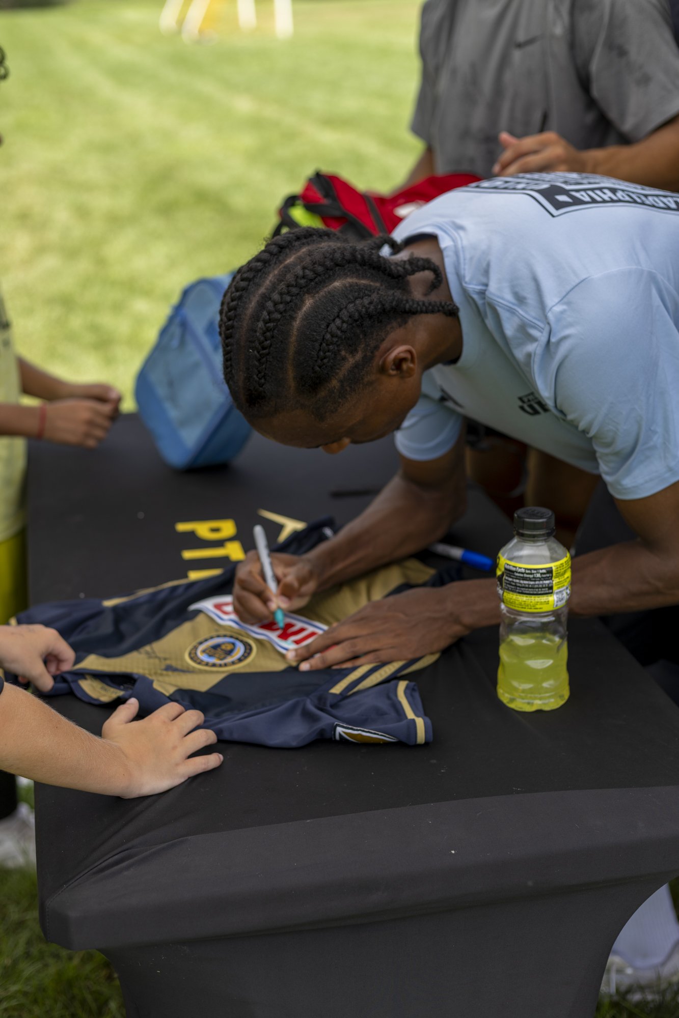 Person signing a sports jersey on a table outdoors, with a water bottle nearby.
