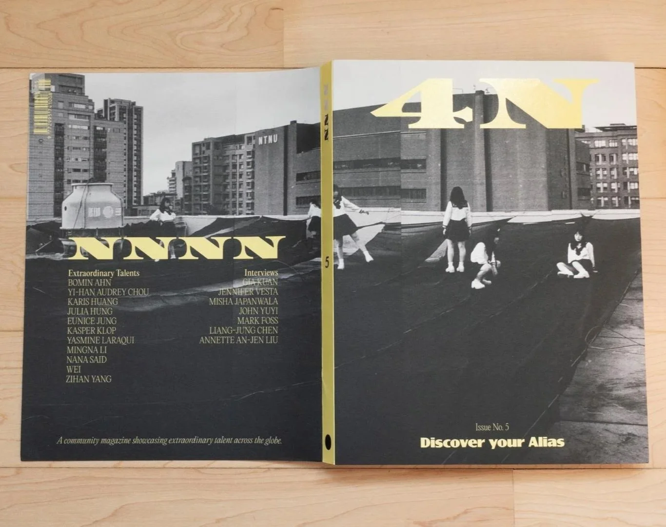 A community magazine opened to reveal black and white photographs of children playing on a rooftop in an urban setting, with tall buildings in the background. The magazine features text about extraordinary talents and interviews, with a headline to discover your alias.