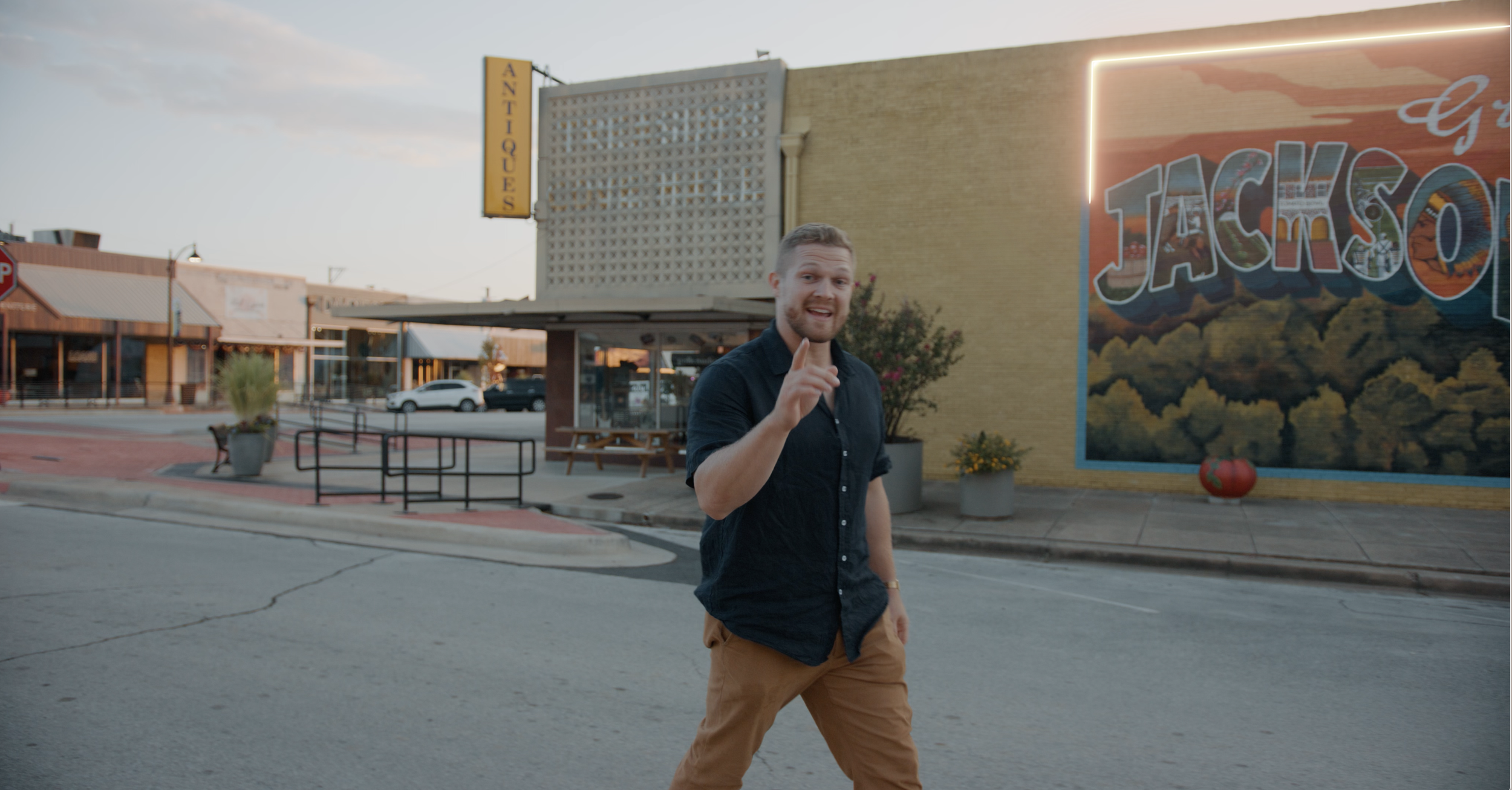 Man walking on a street in front of a mural and antique store in a small town.