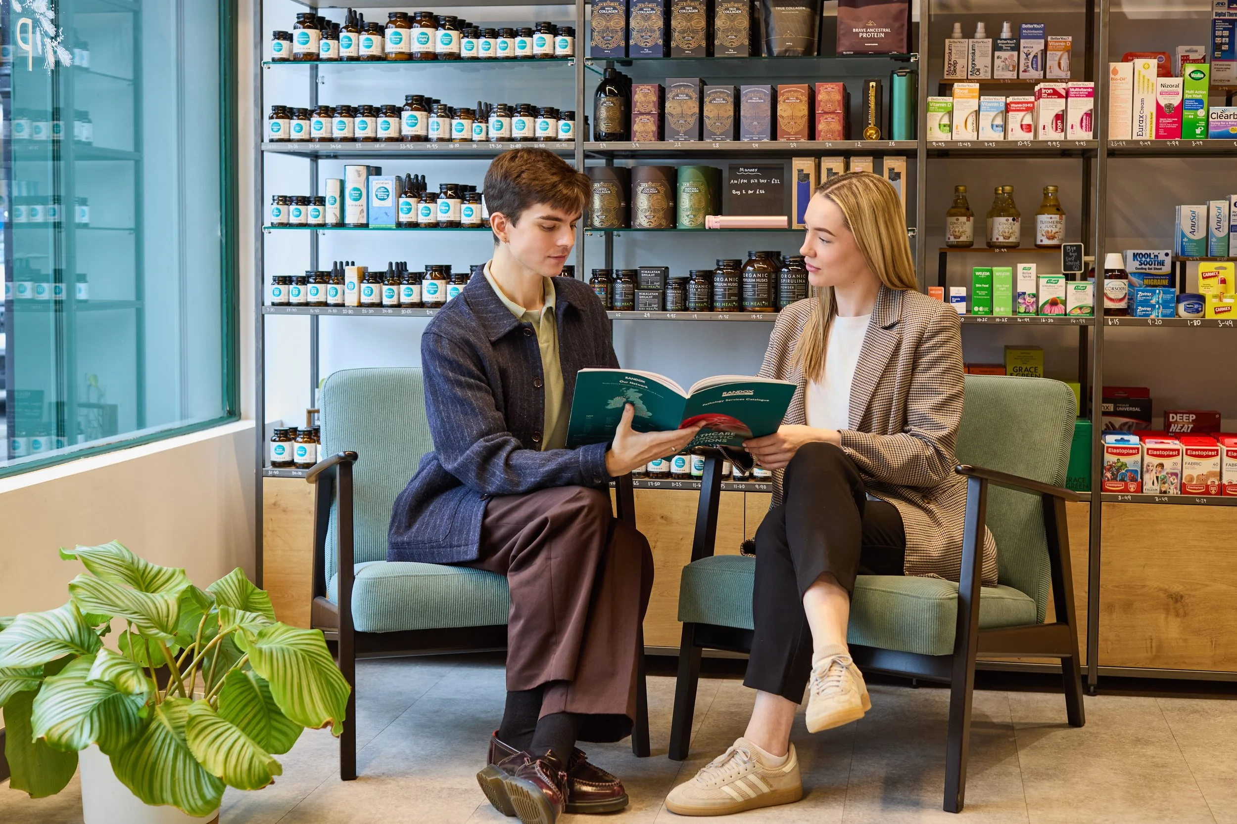 Woman sitting on a wooden cabinet, smiling, with abstract colorful paintings on the wall behind her, and a large white round vase on the cabinet.