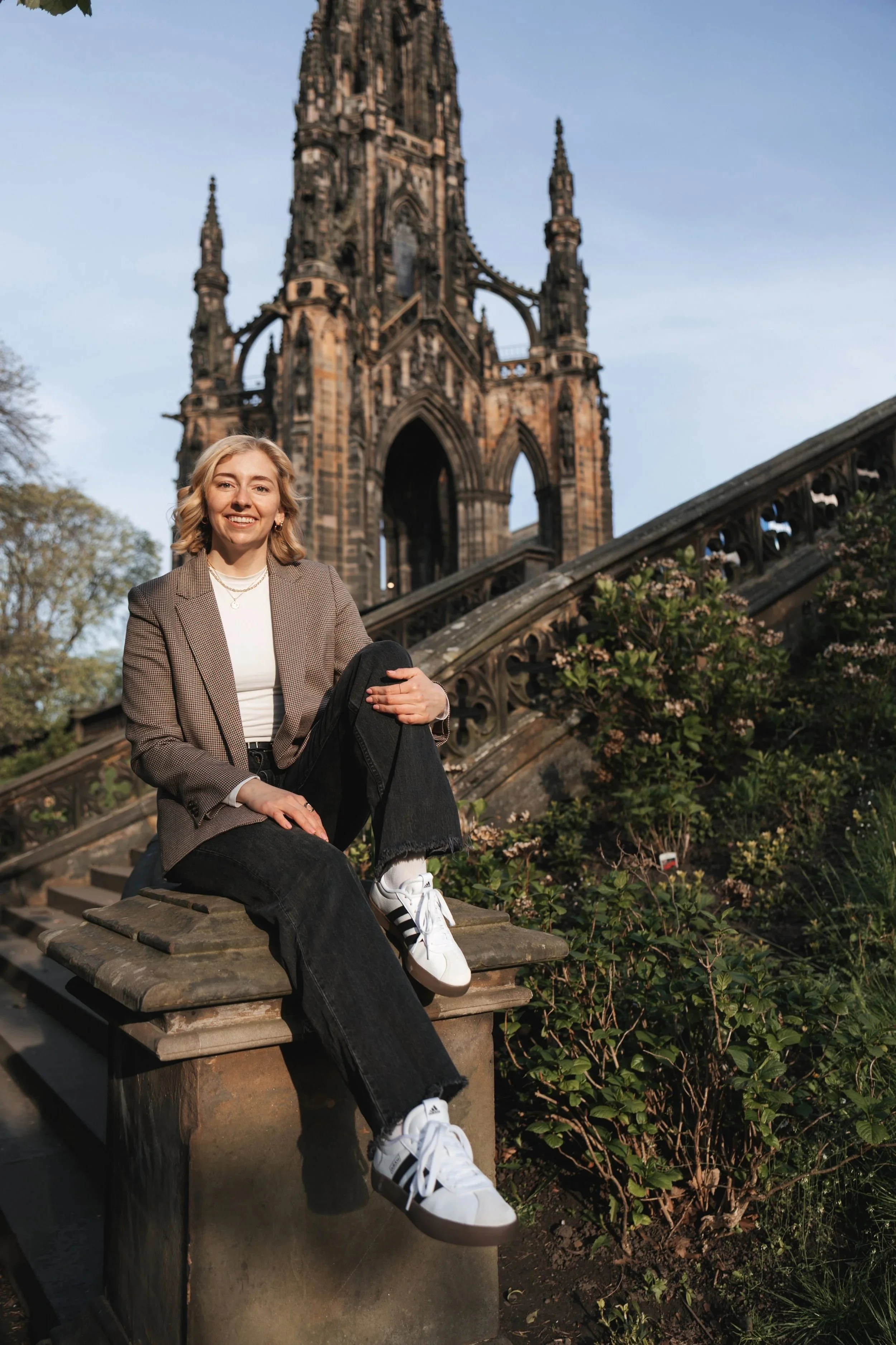 Person sitting on pillar in front of Scott Monument in Edinburgh.