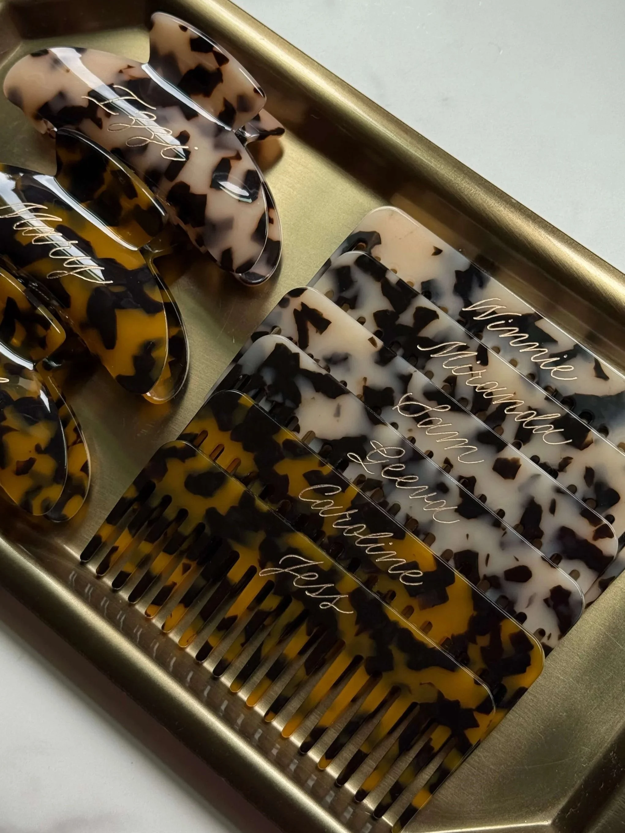 Hand engraved tortoise shell pocket combs and hair claw clips, personalized with names in elegant modern calligraphy style and gold lettering. 