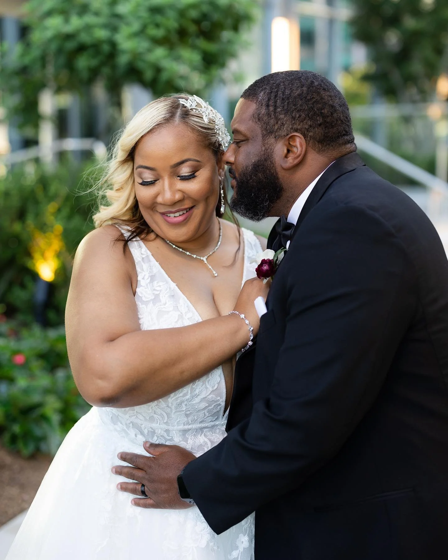 A bride and groom share an intimate moment outdoors, smiling and embracing on their wedding day.
