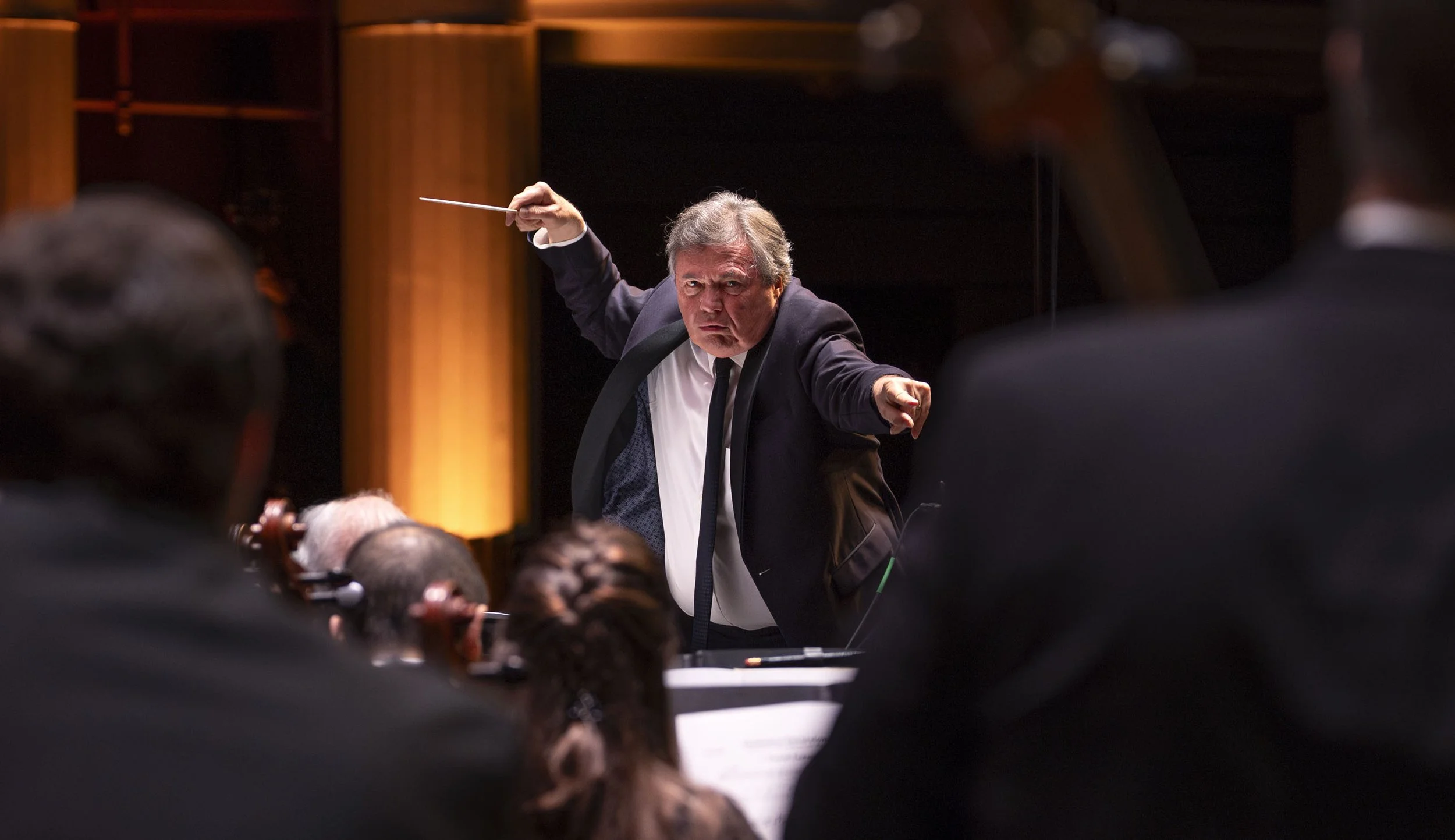 An orchestra conductor, an older man in a suit, passionately directing an orchestra during a performance.