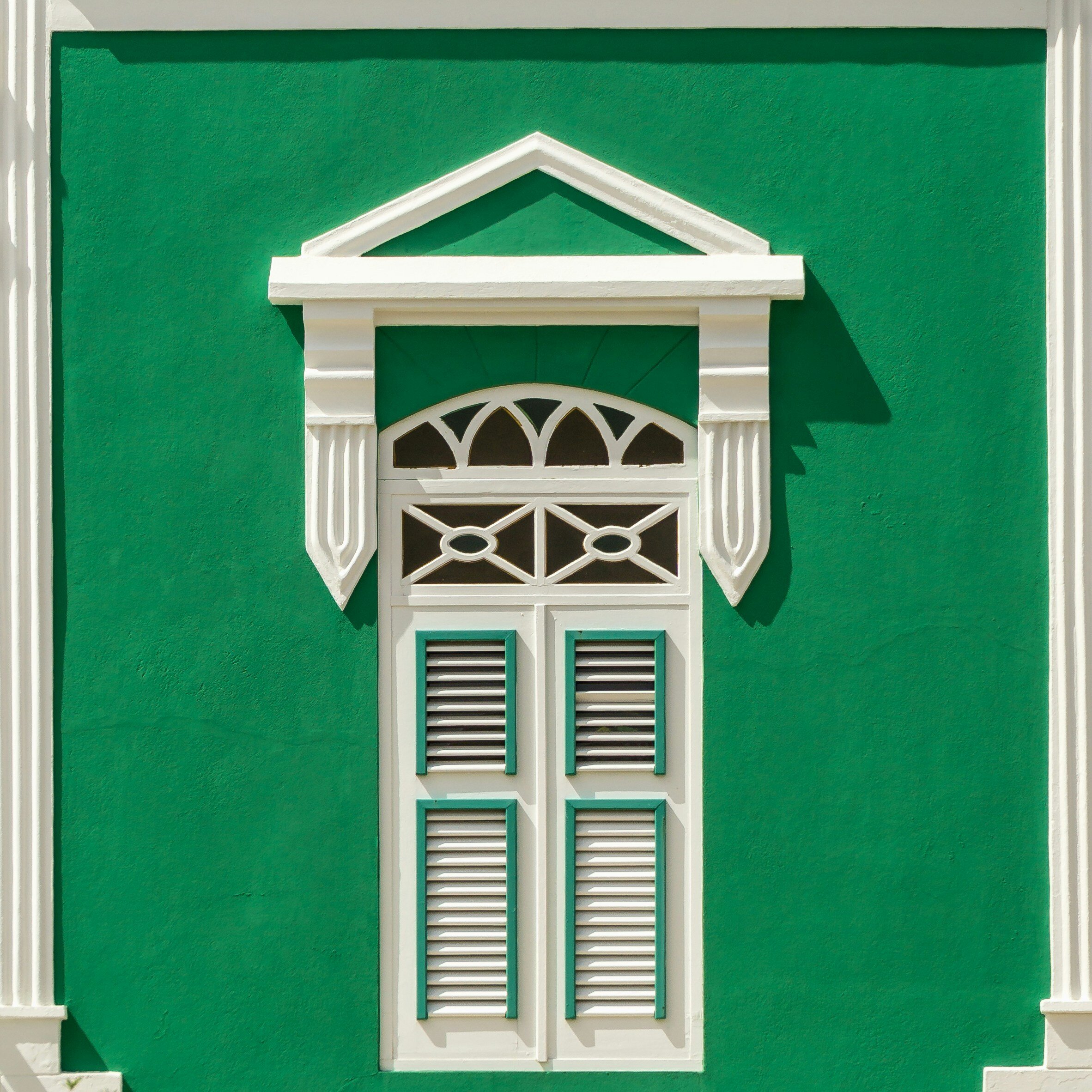 Decorative green wall with white window shutters and architectural trim, resembling a classical façade.