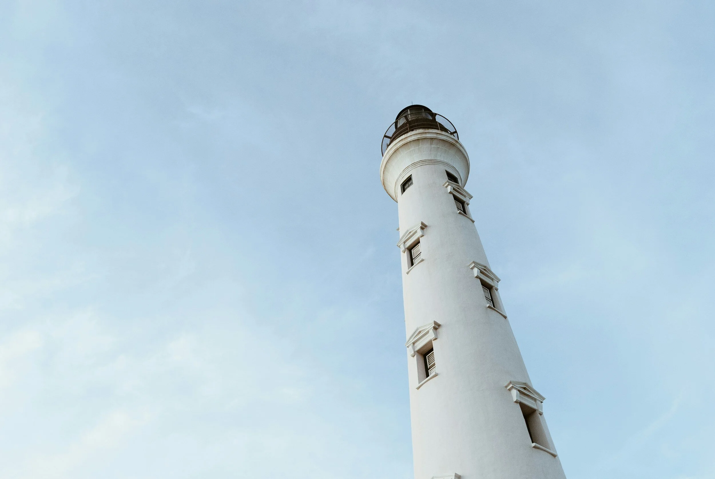 A white lighthouse under a clear sky with a few clouds.