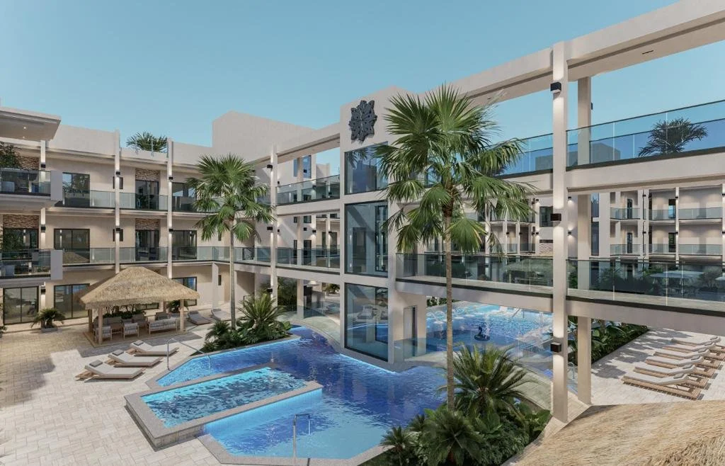 View of a modern hotel courtyard featuring a swimming pool, palm trees, and lounge chairs under umbrellas, with apartment balconies surrounding the area.