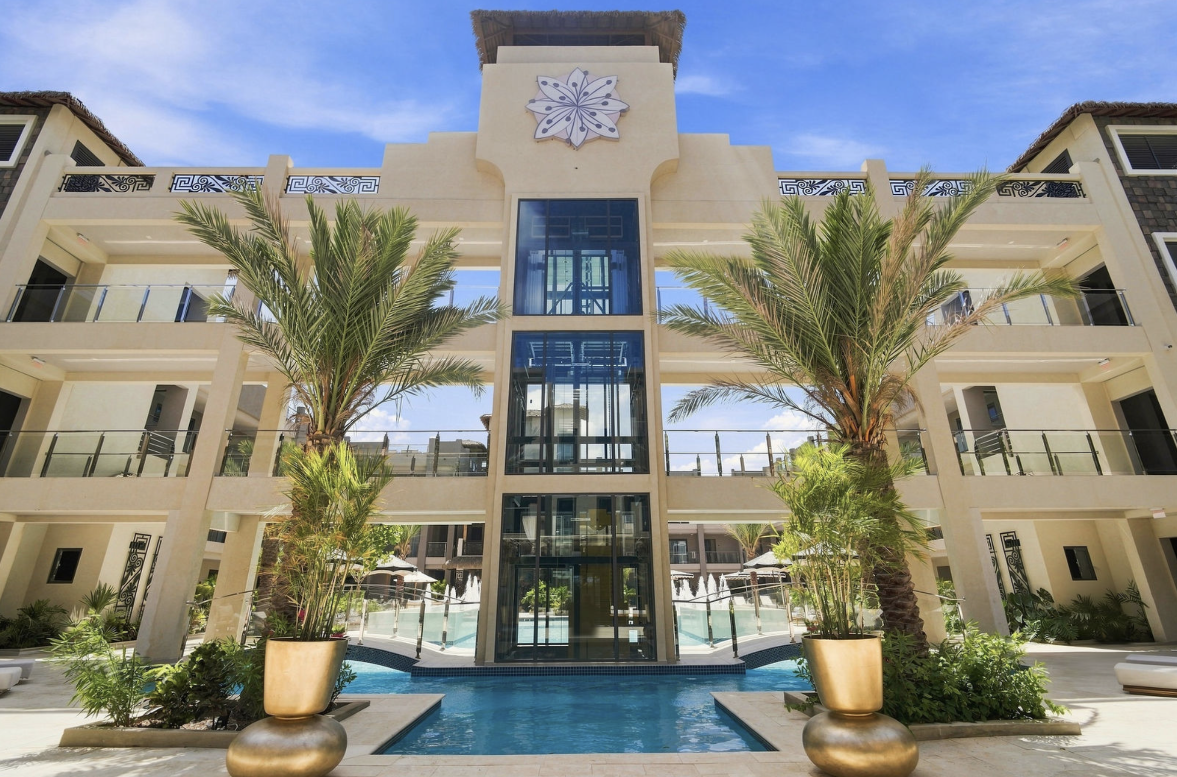 Luxury hotel courtyard with a central water feature, surrounded by palm trees and modern architecture, under a clear blue sky.