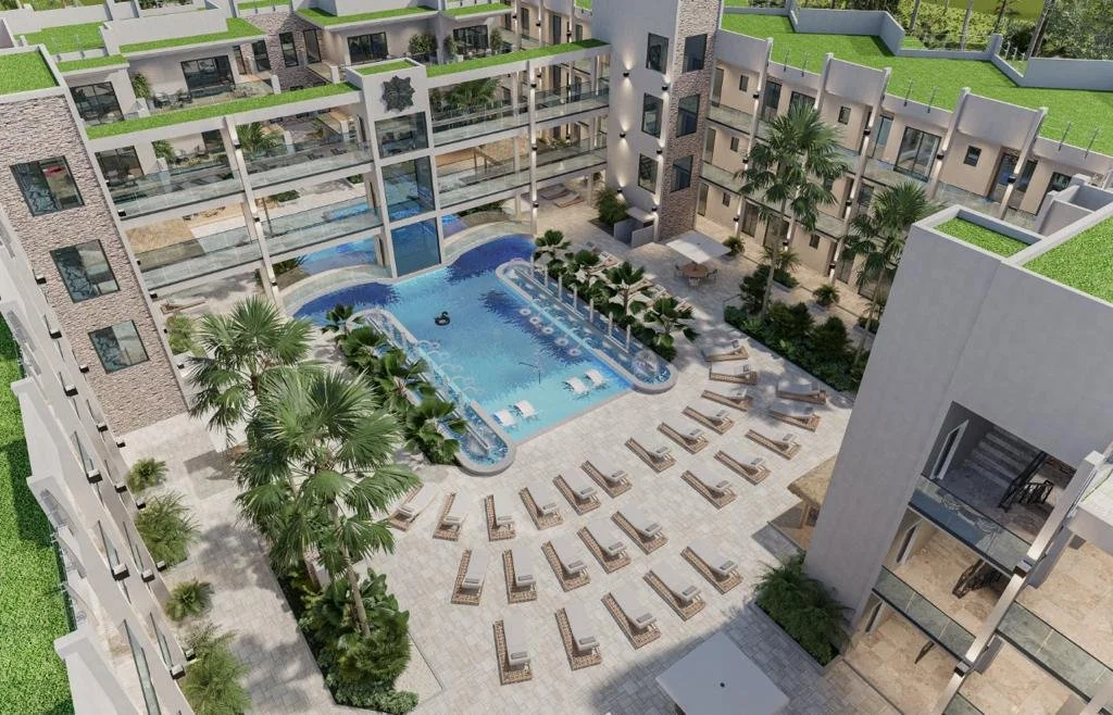 Aerial view of a modern residential apartment complex with a central swimming pool, surrounded by lounge chairs, palm trees, and landscaped greenery.