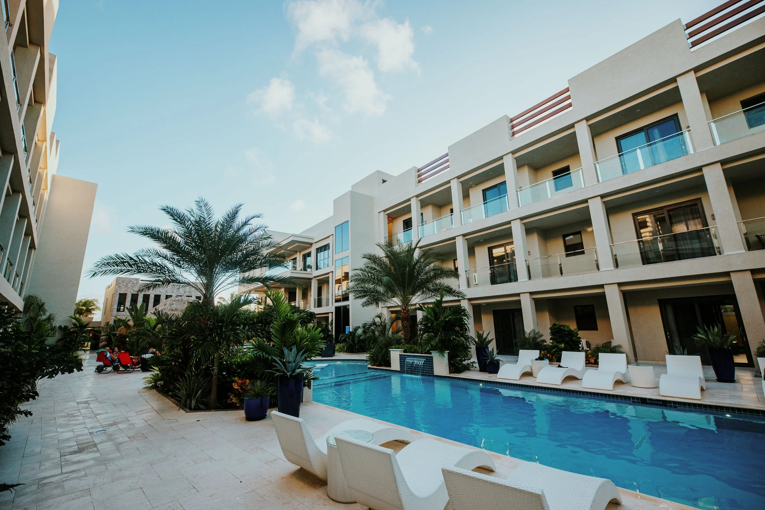 Pool area with lounge chairs and palm trees at a modern apartment complex under a cloudy sky.