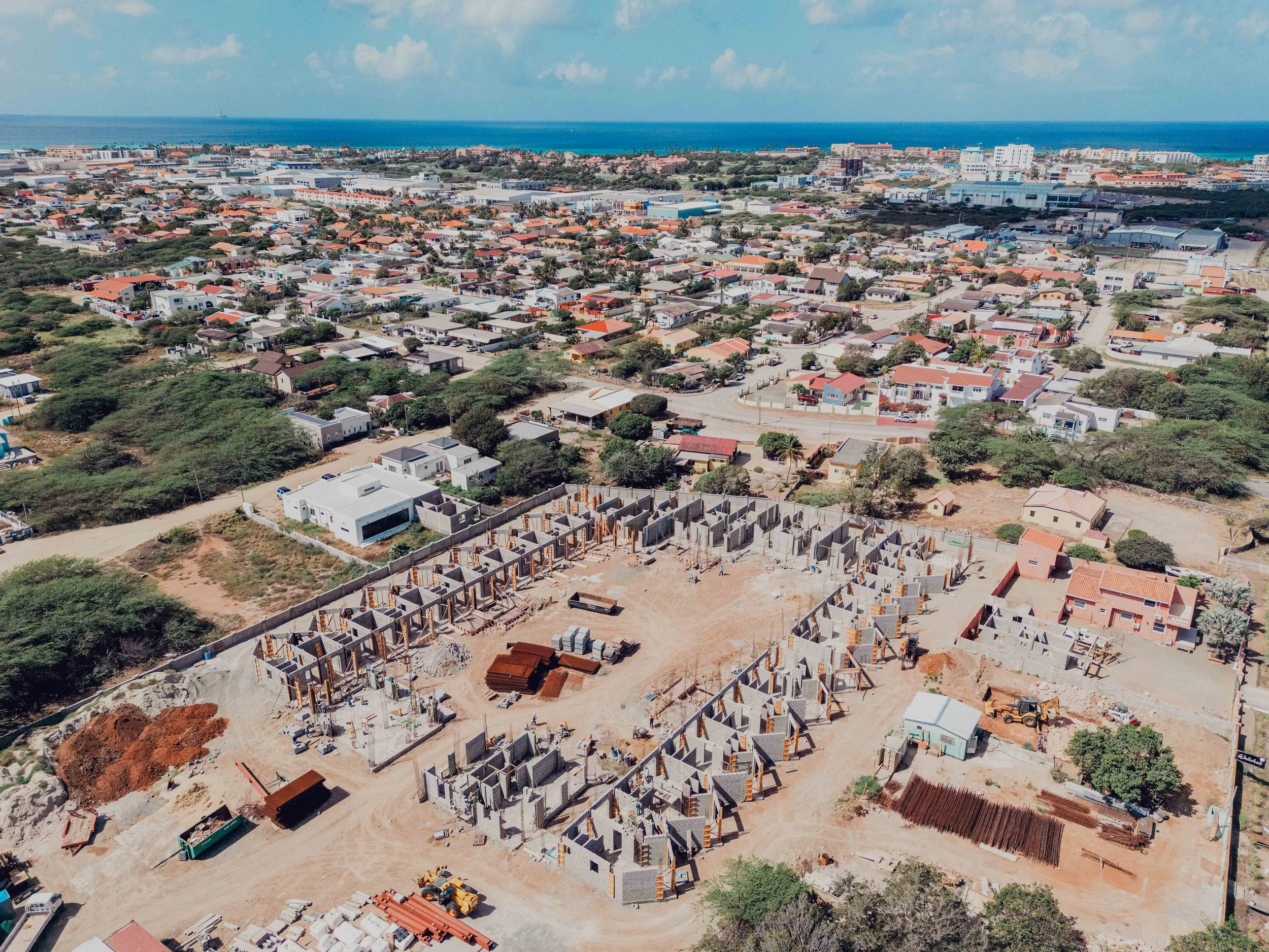 Aerial view of a construction site with multiple house foundations being built, surrounded by a residential neighborhood near the coast.