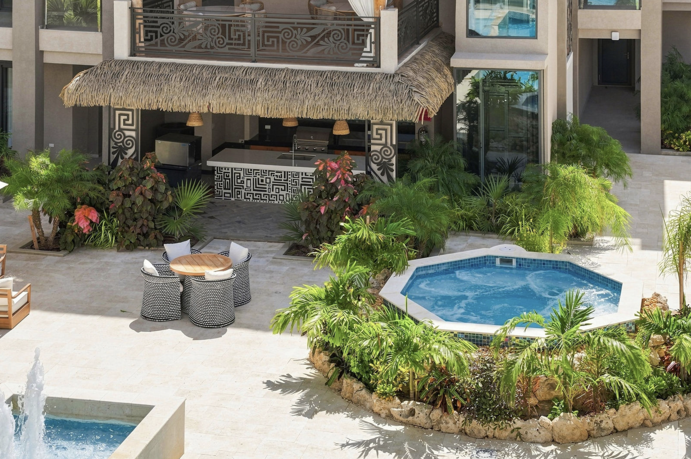 A luxurious vacation resort with a swimming pool, lush tropical plants, and an outdoor bar area with thatched roof and decorative black-and-white patterns.