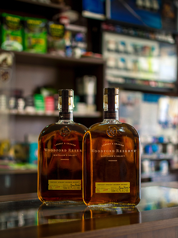 Professional product photography of two bourbon bottles reflecting on a polished countertop in a dimly lit bar