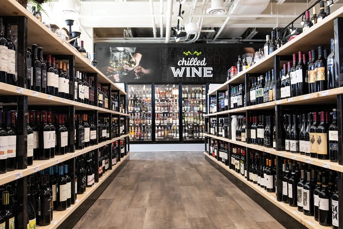 A wine store aisle with shelves of wine bottles on both sides and a sign that says 'chilled WINE' above the refrigerated section at the back.