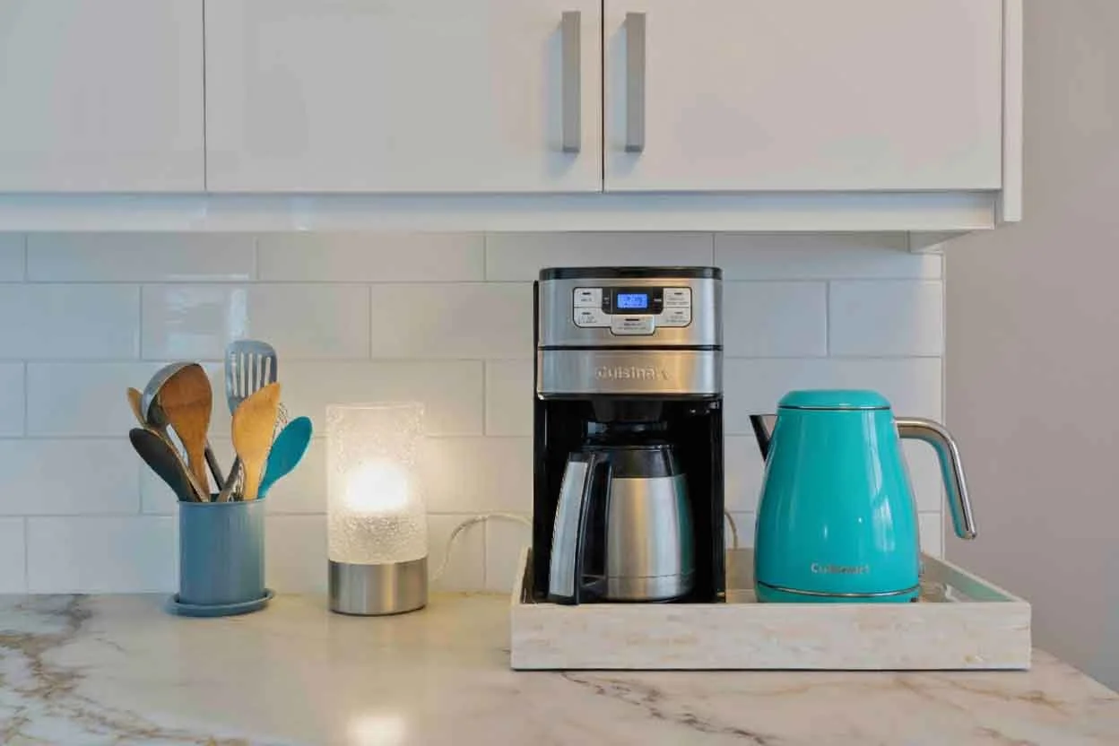 Countertop with a utensil holder, a small light, a coffee maker, and a teal electric kettle.