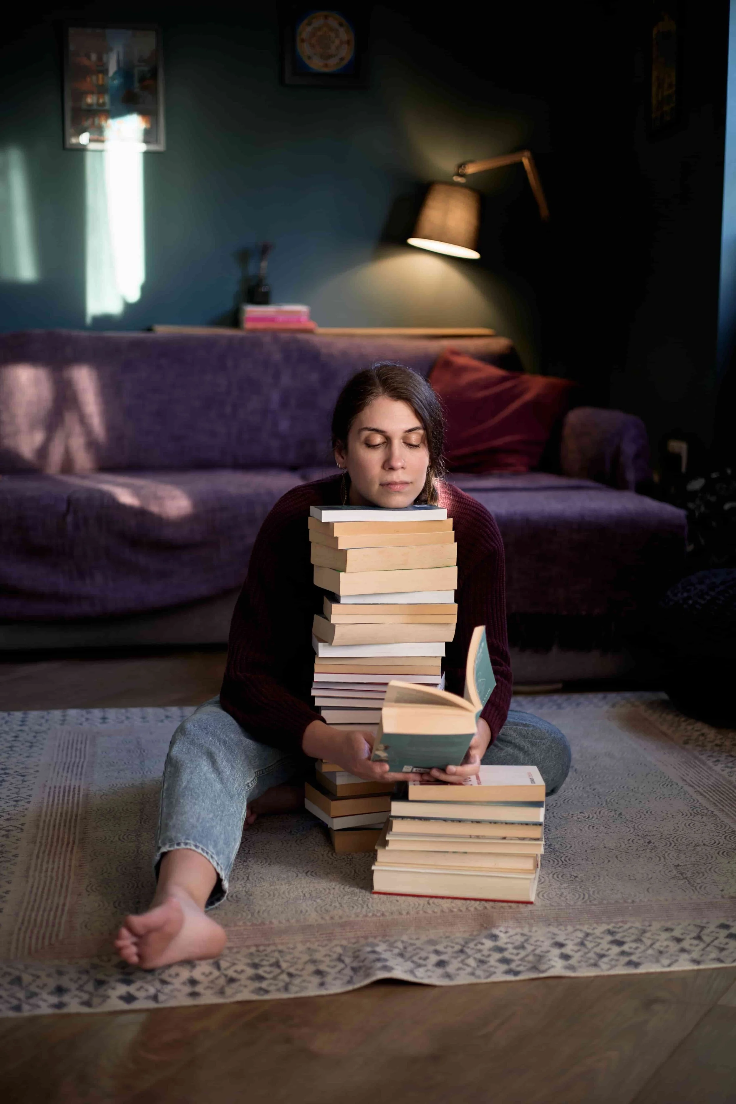 Carina, LGBTQIA+-affirming CBT therapist, sitting on the floor resting her head on a pile of books, reading
