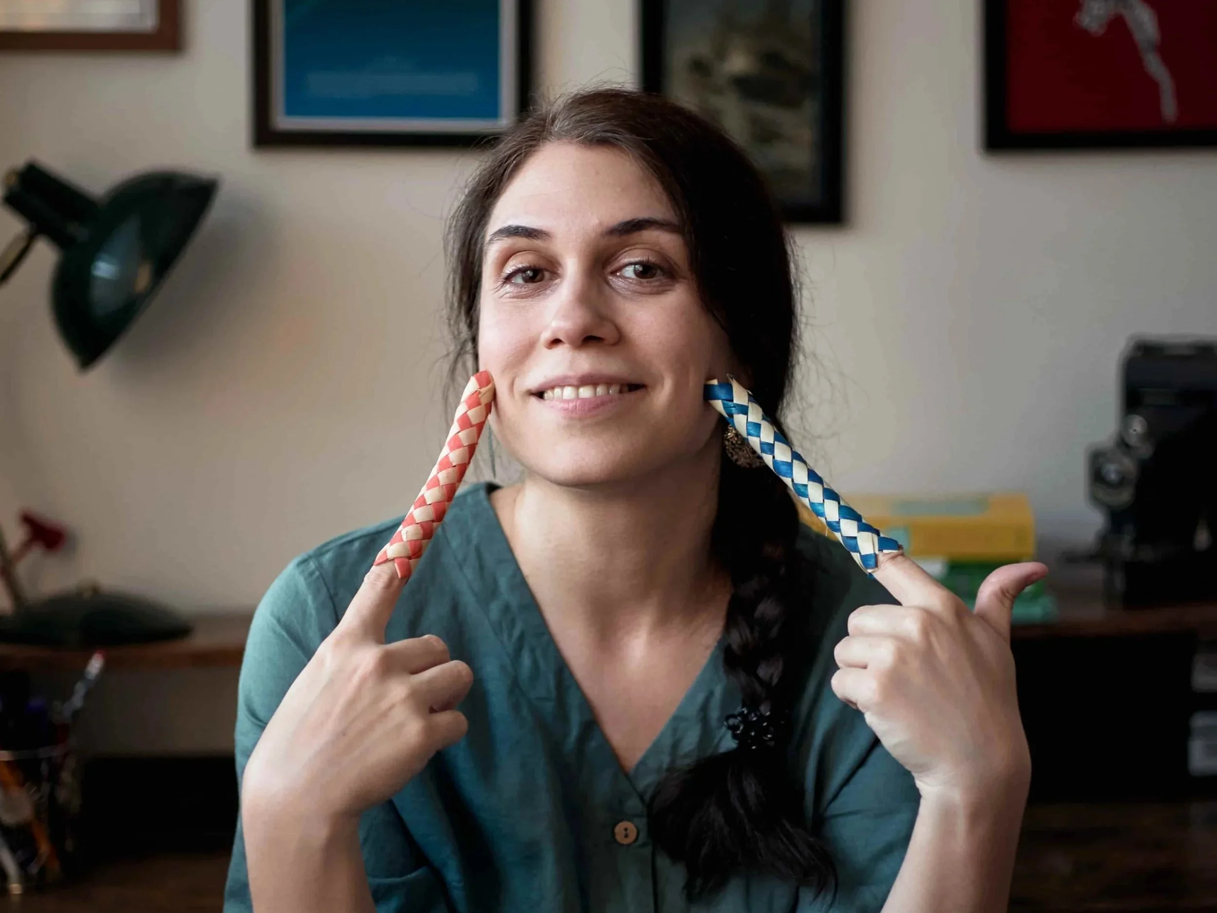 Carina, a neurodivergent-affirming therapist, smiling at the camera while holding Chinese fingers traps on each of her index fingers and using these to touch her face