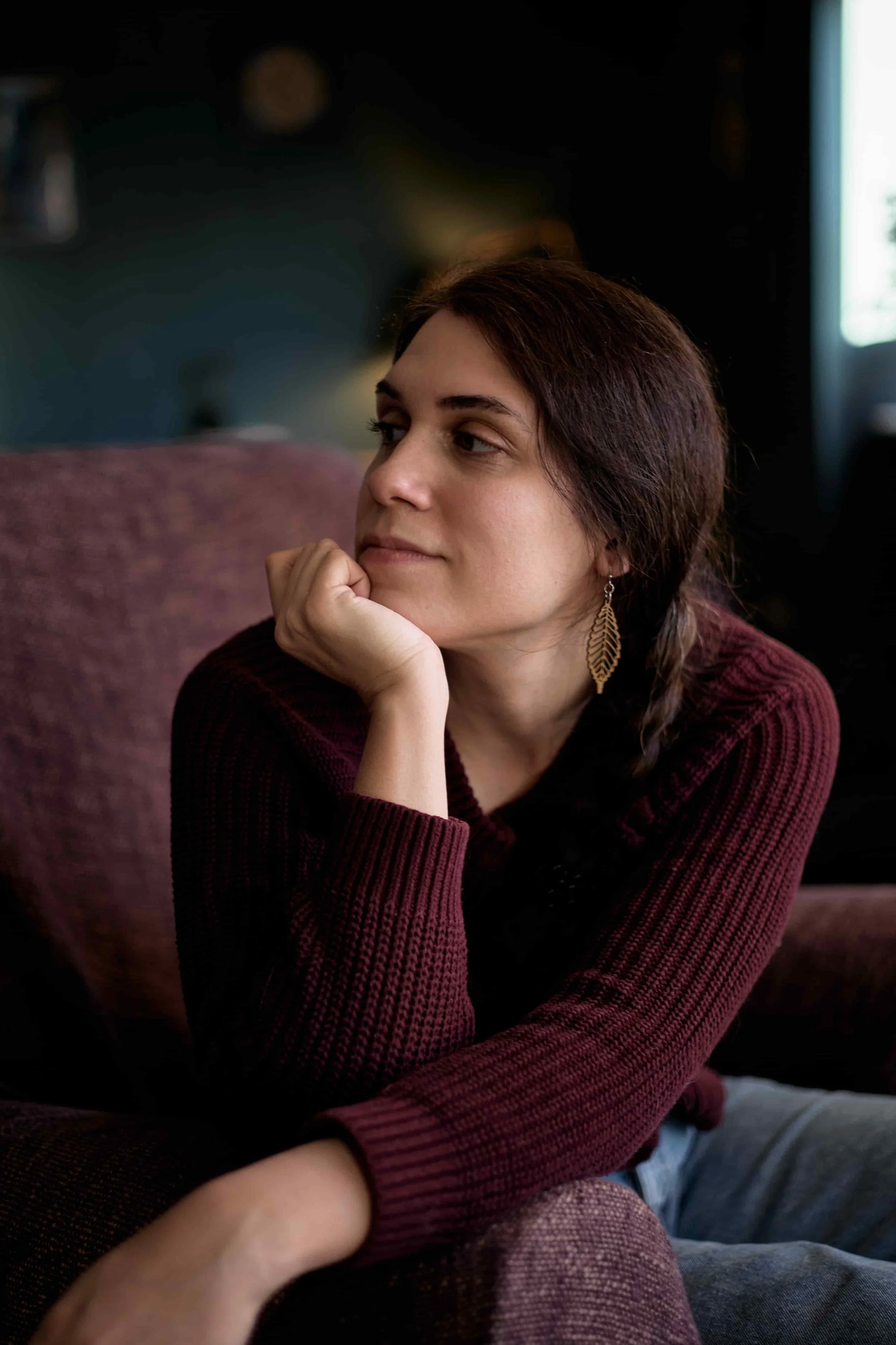 Carina, a therapist offering online intensive therapy for high-achievers, sitting on an armchair wearing a burgundy jumper, resting chin in hand