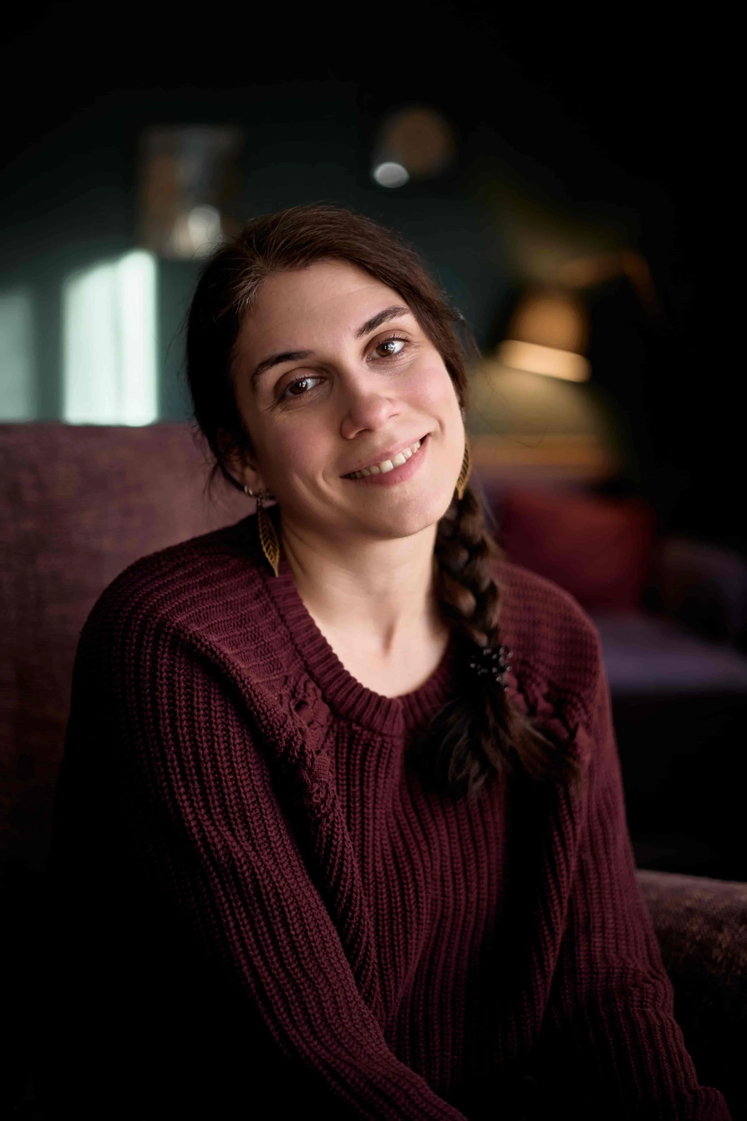 Carina, a high-functioning anxiety therapist, wearing a burgundy jumper and dark hair in a braid, smiling at the camera