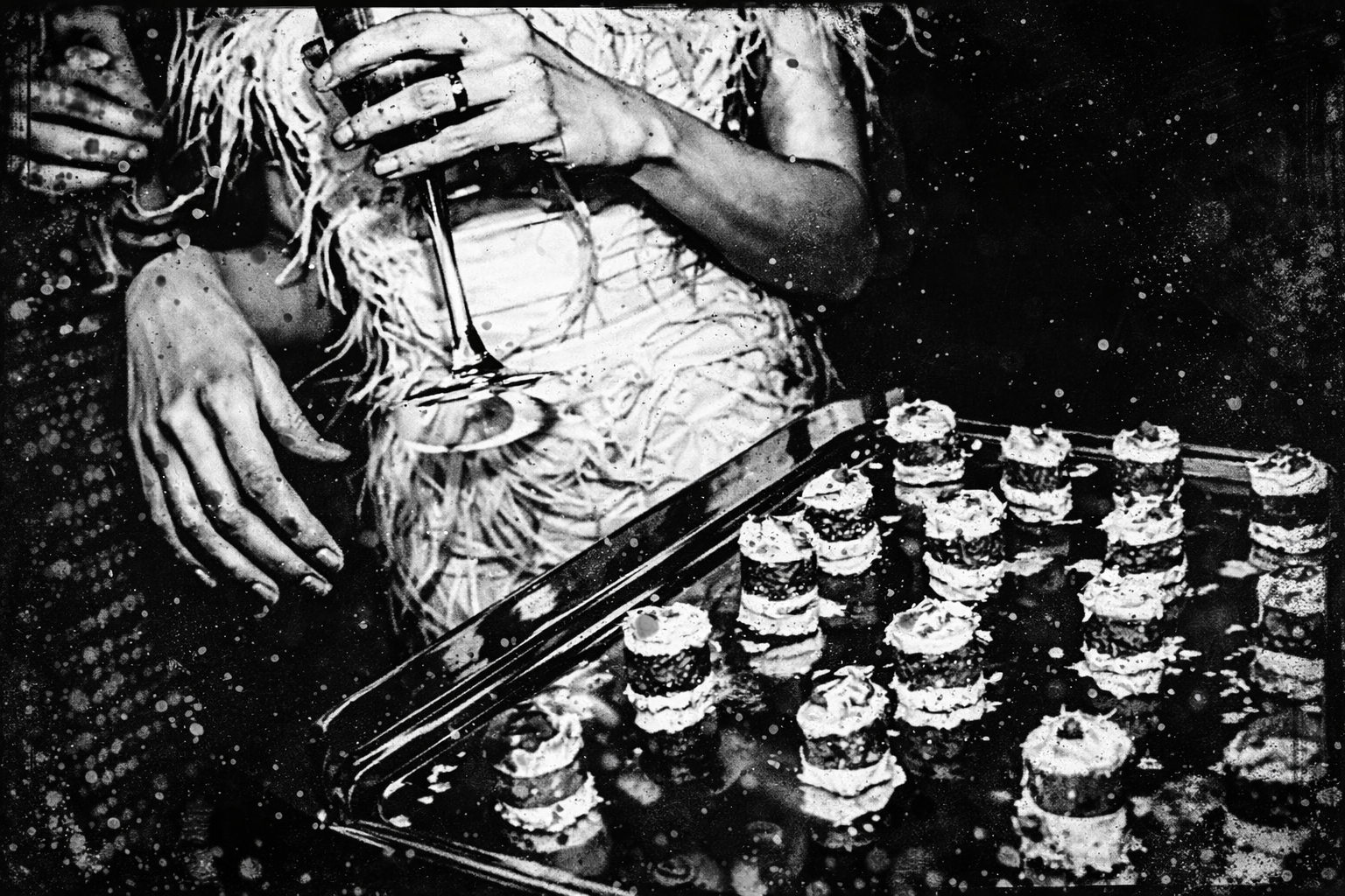 A person holding a glass of champagne next to a tray of small, layered appetizers or desserts, likely at a party or celebration.