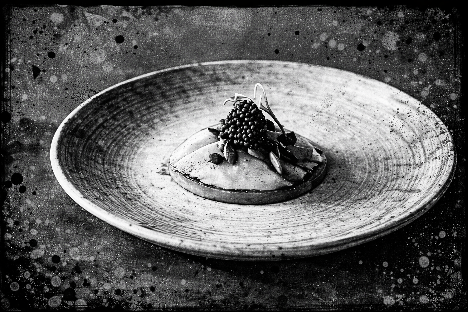 A plated gourmet dish with a piece of white fish topped with black caviar and microgreens, served with a sauce on an oval ceramic plate.