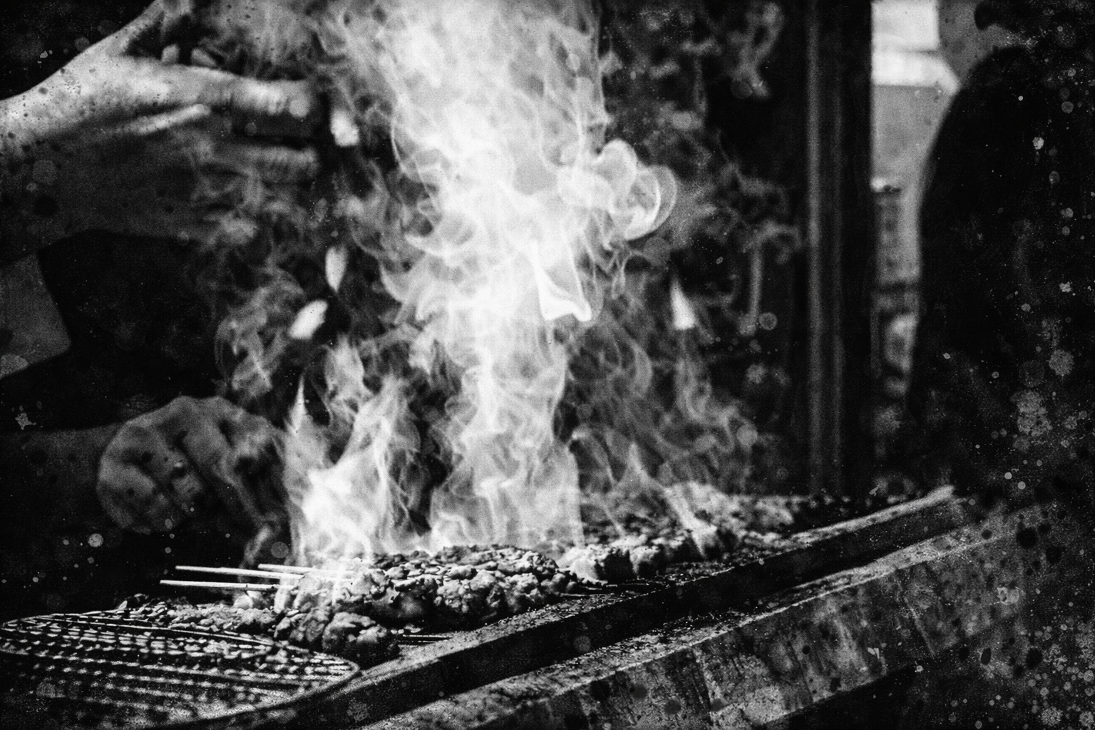 A chef grilling meat on a barbecue grill with flames and smoke.
