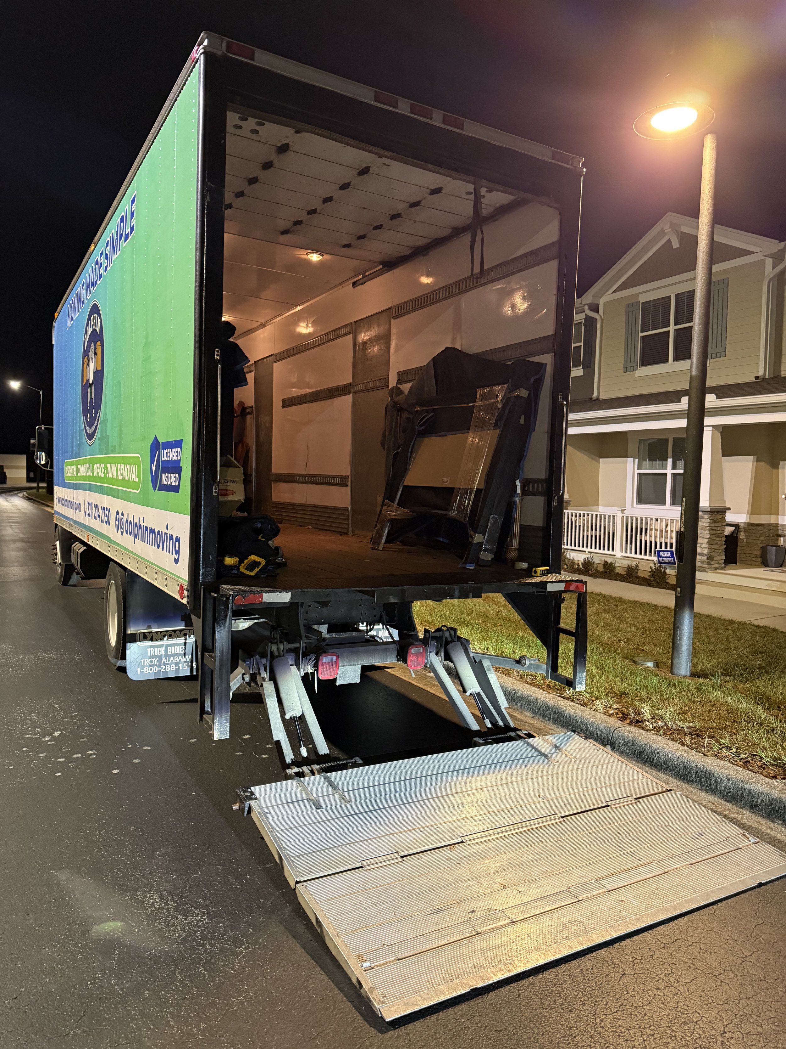 Empty moving truck with a lowered ramp parked on a residential street at night.