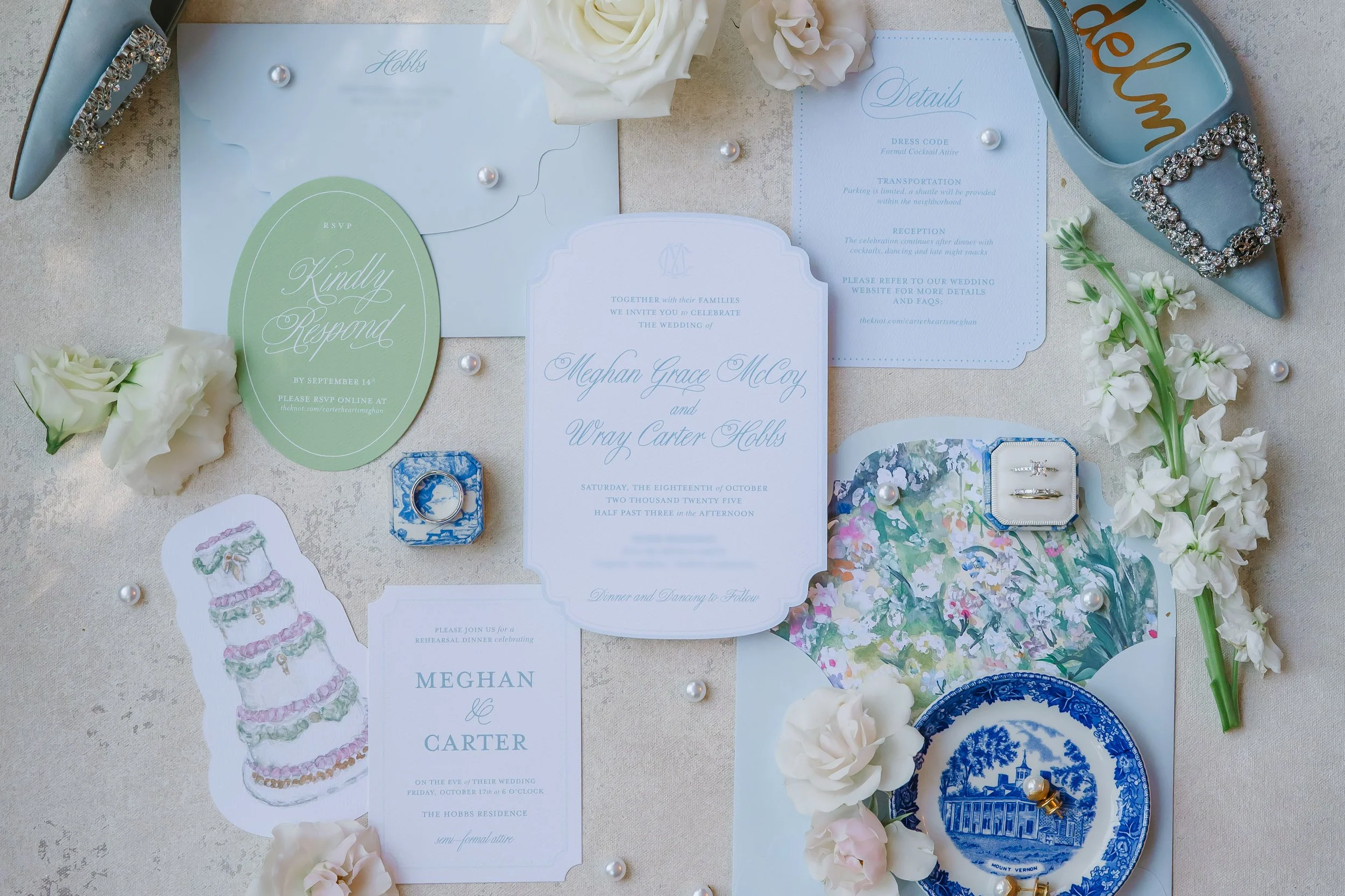 Wedding invitation suite and accessories, including rings, flowers, and decorative elements, arranged on a light-colored table.