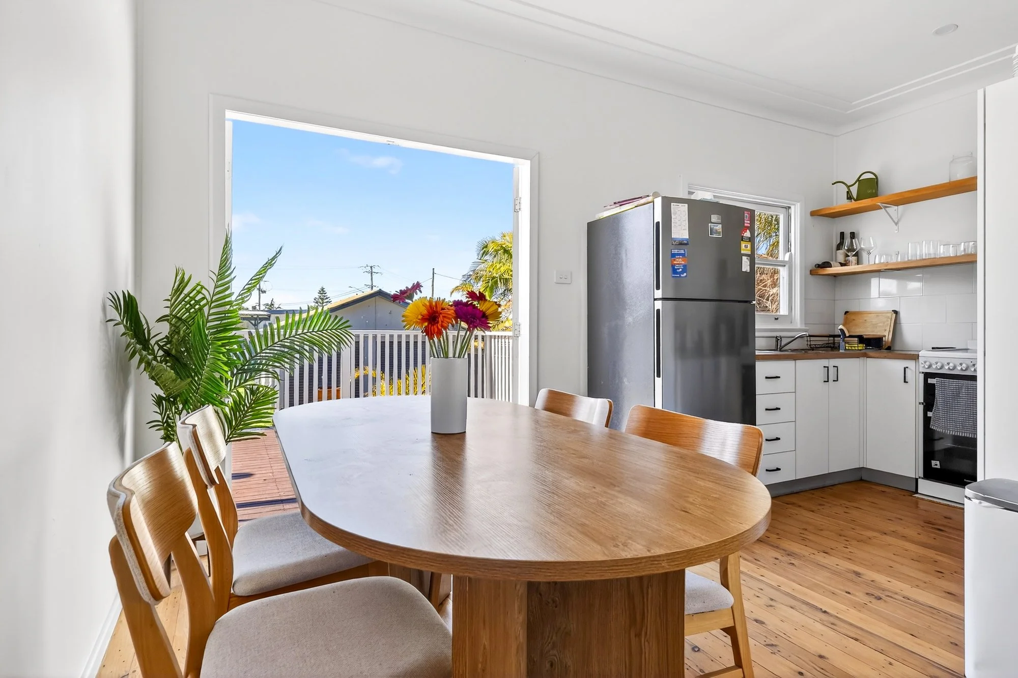 Kitchen with a dining table, chairs, a potted plant, and a vase of flowers, with a view of a deck outside.