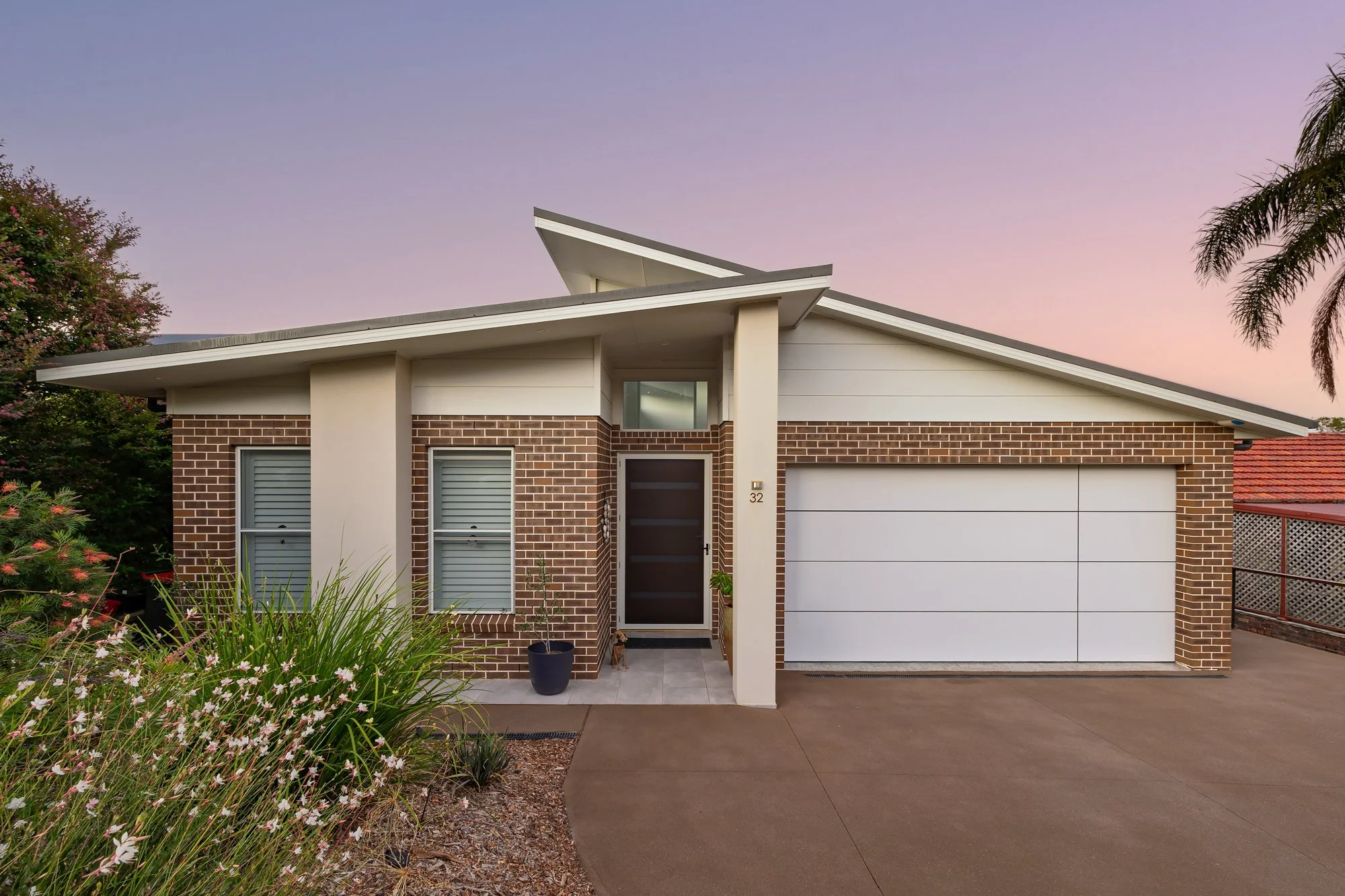 Modern brick house with white accents, a garage, and a small front porch at dusk.