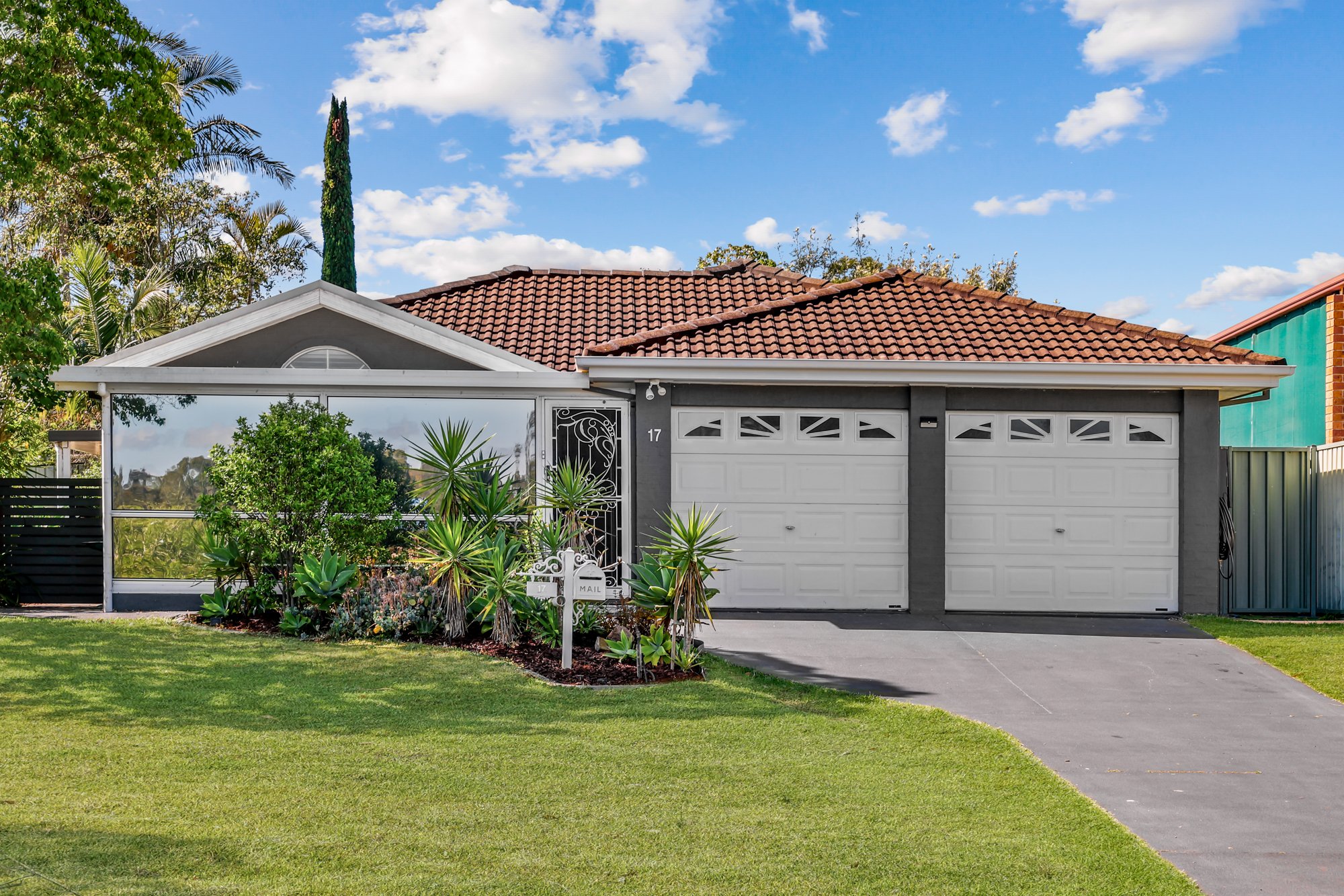 Modern single story home with double garage and tidy lawn and gardens. The property is rendered is slate grey with dark roof and white roller doors and front doors. Captured for real estate listing by Prestige Property Photography.