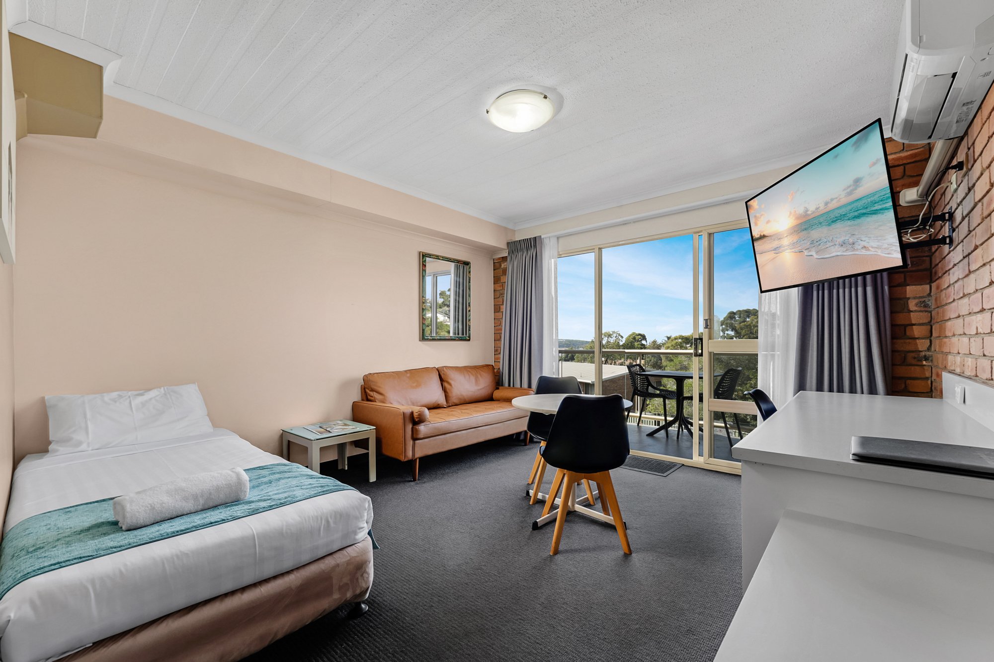 Spacious hotel suite bedroom with single bed, modern finishes, and balcony view.