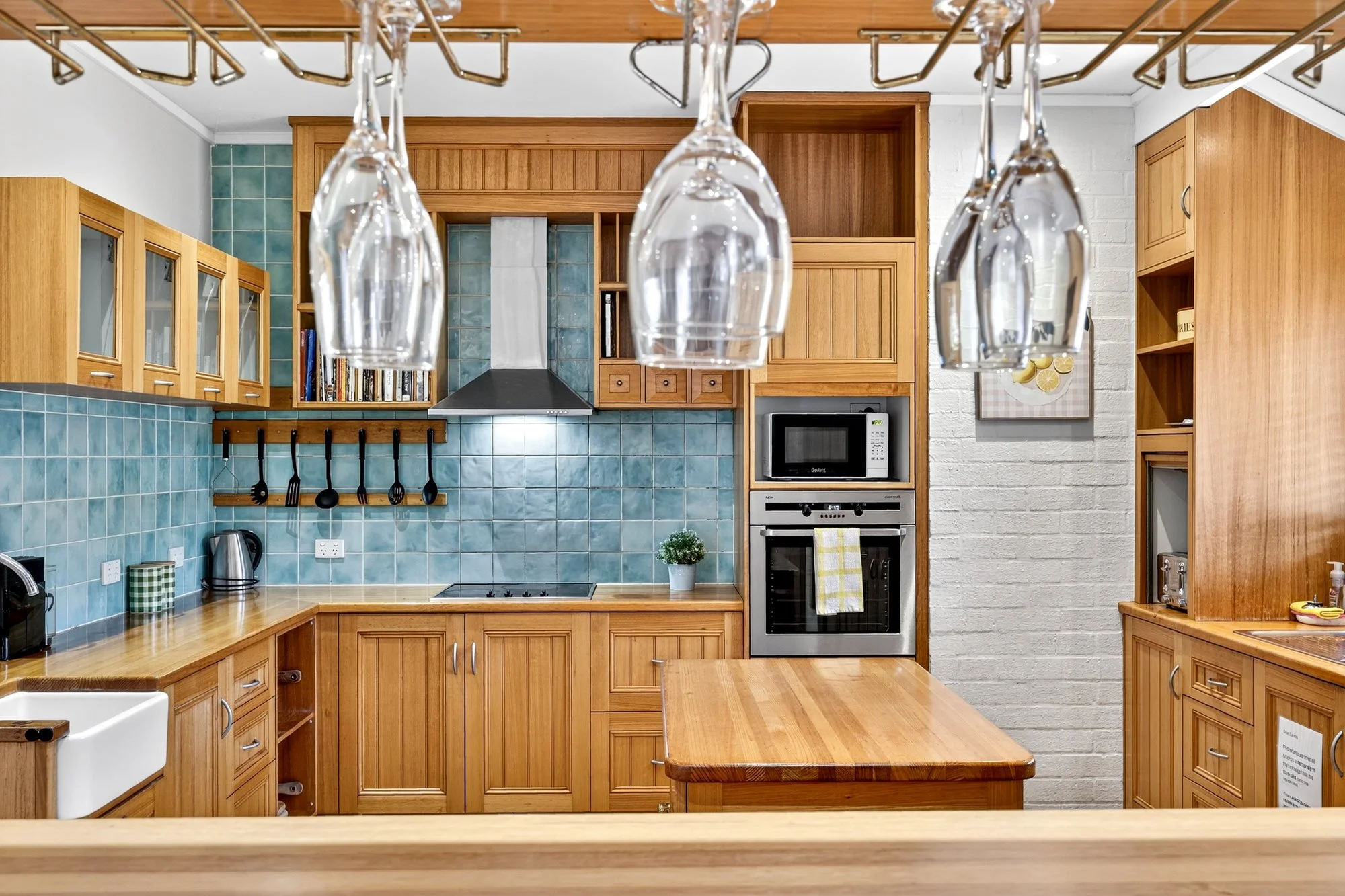 Kitchen with wooden cabinets, blue tiled backsplash, stainless steel appliances, and hanging wine glasses above the counter.