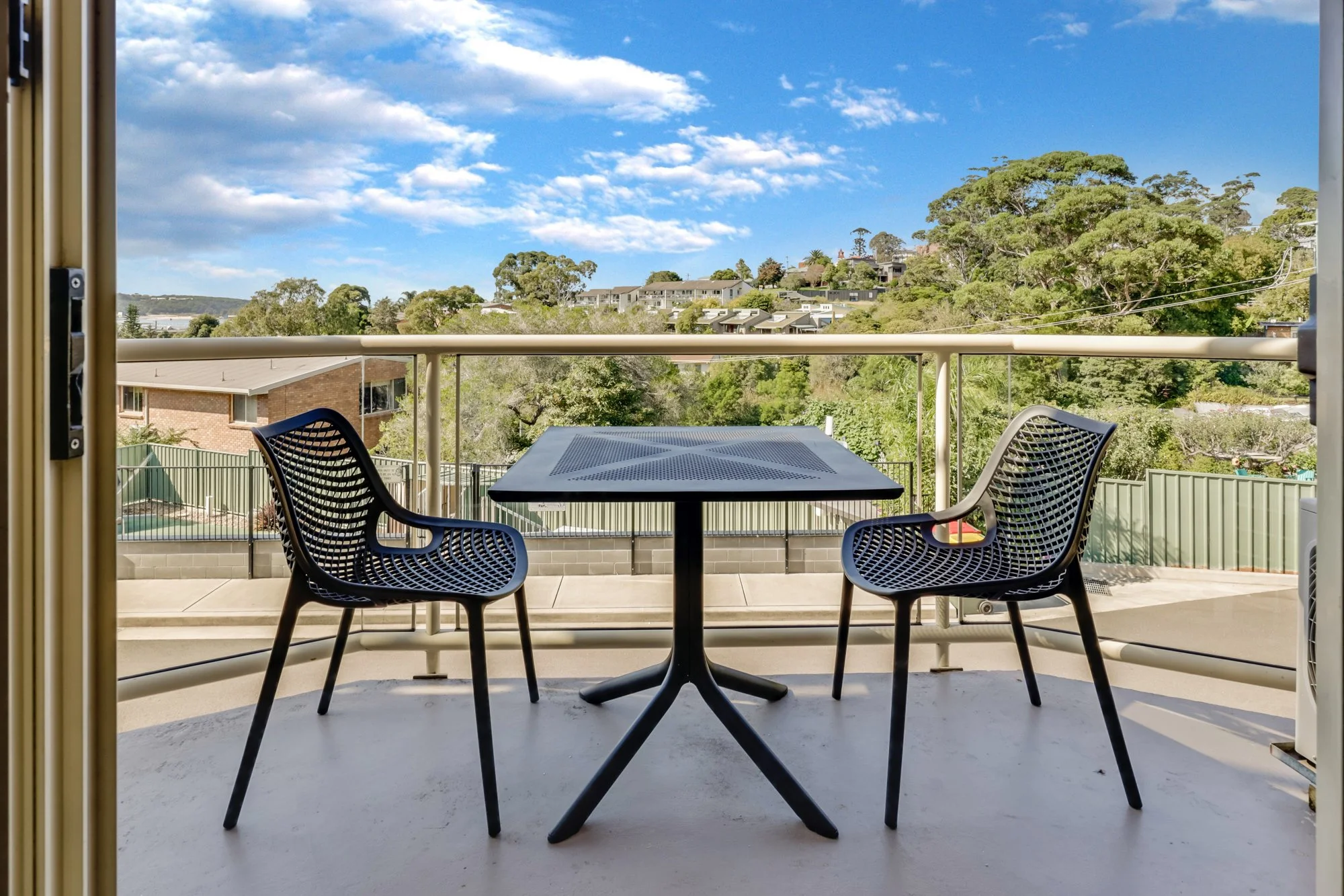 Hotel Photography. Balcony view. Gardens and blue sky from the view of the outdoor table and chairs.