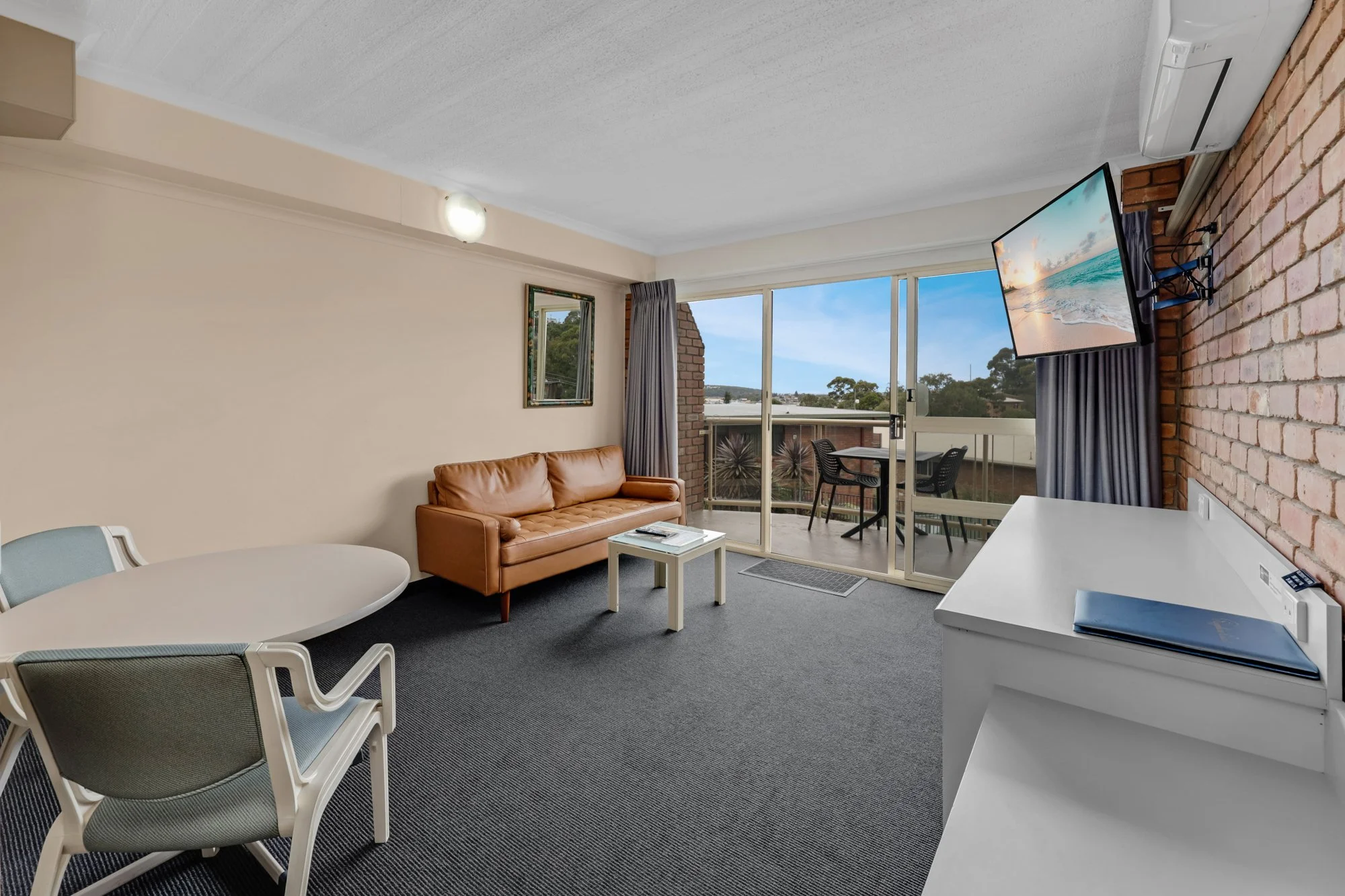 Spacious hotel suite bedroom with coffee coloured leather lounge, modern finishes, and balcony view. Hotel Photography