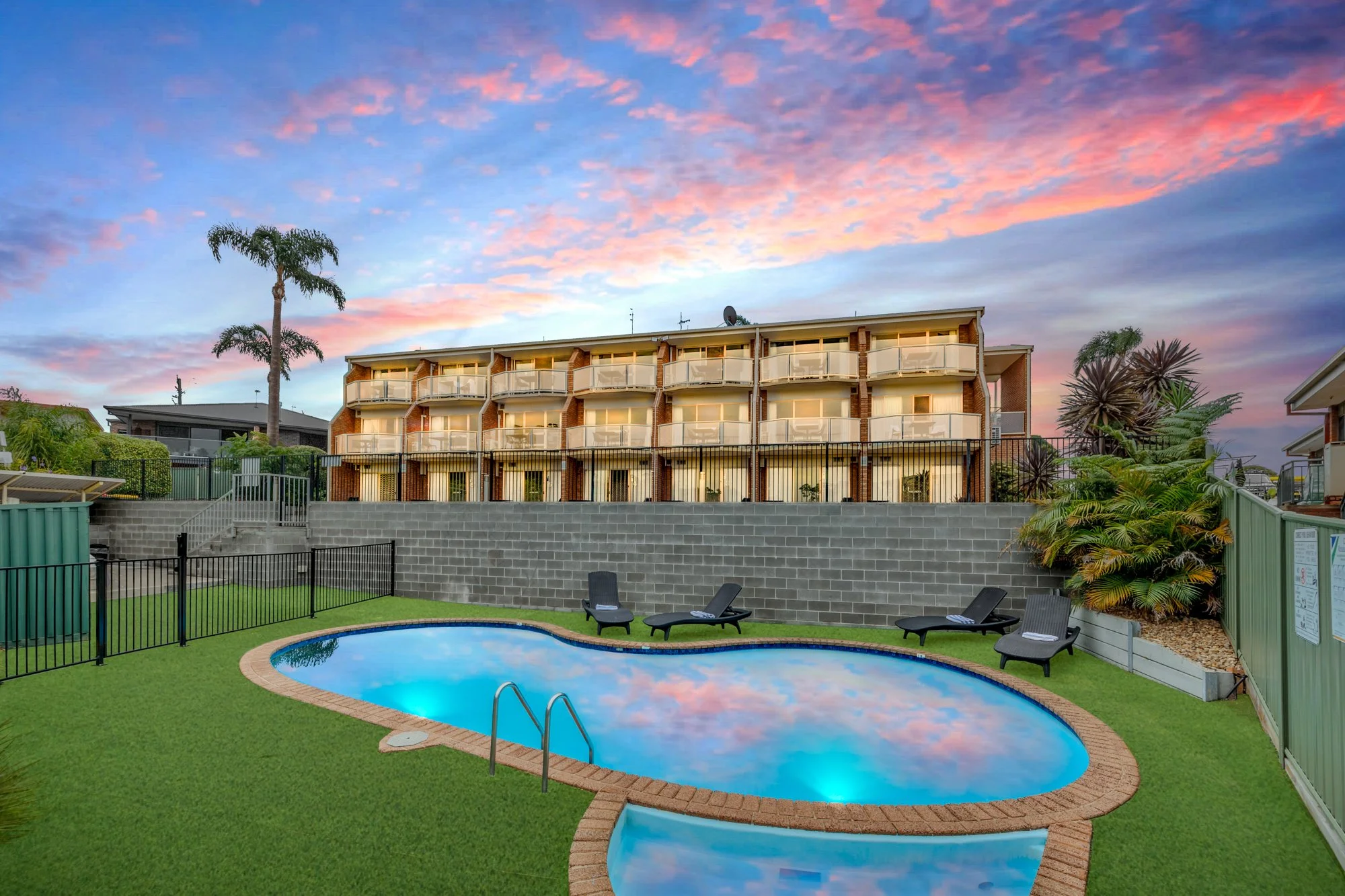 Hotel Photography. Twilight hero shot of the pool to hotel with sky reflections in the pool and artificial turn and gardens and palm trees.