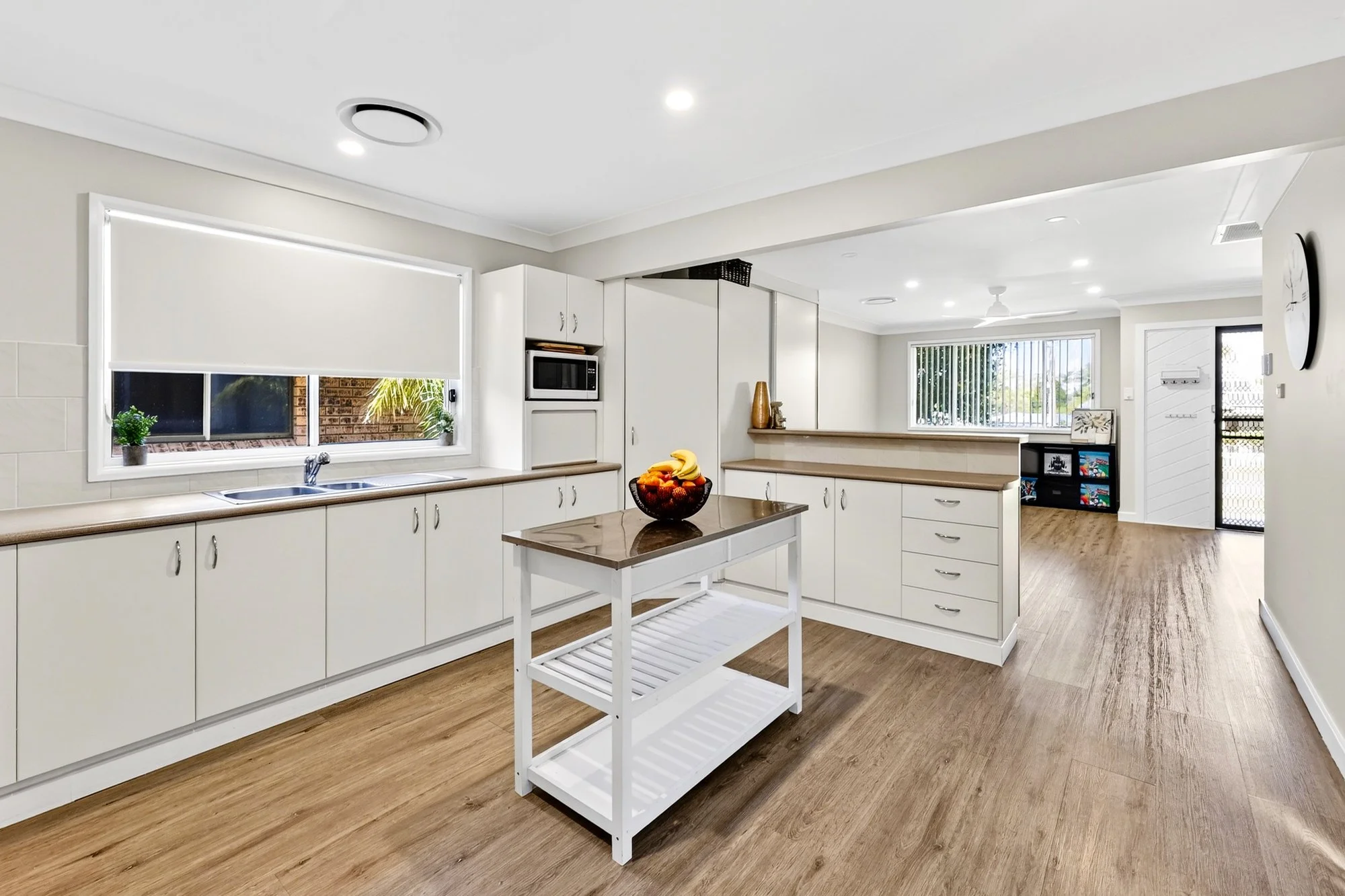 Modern kitchen with white cabinets, wooden countertops, a small kitchen island, a window with blinds, and wooden flooring.