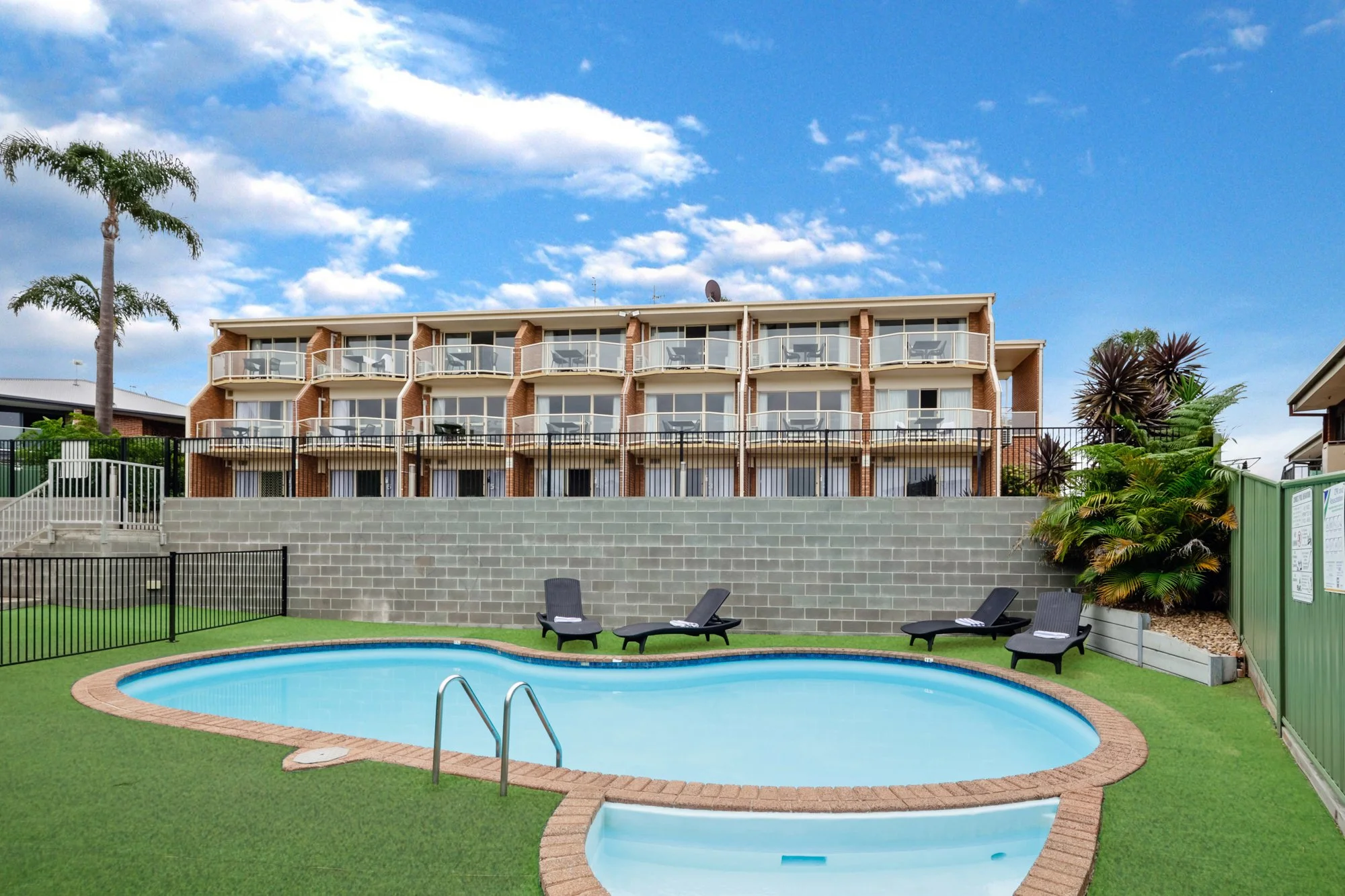 Hotel Photography.Outdoor hotel pool surrounded by lounge chairs and tropical greenery. Hero shot of the hotel in the background.