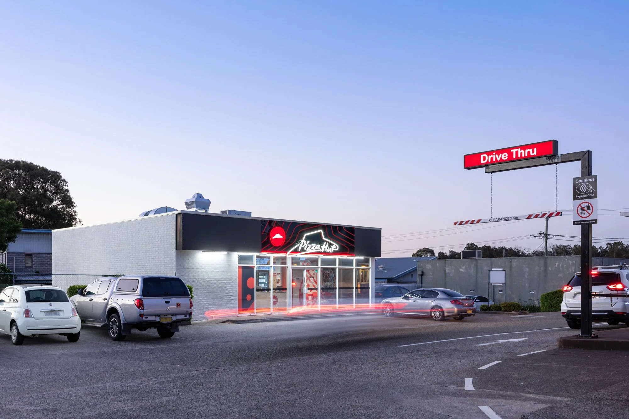 Parking lot at dusk with a Pizza Hut restaurant and a drive-thru sign